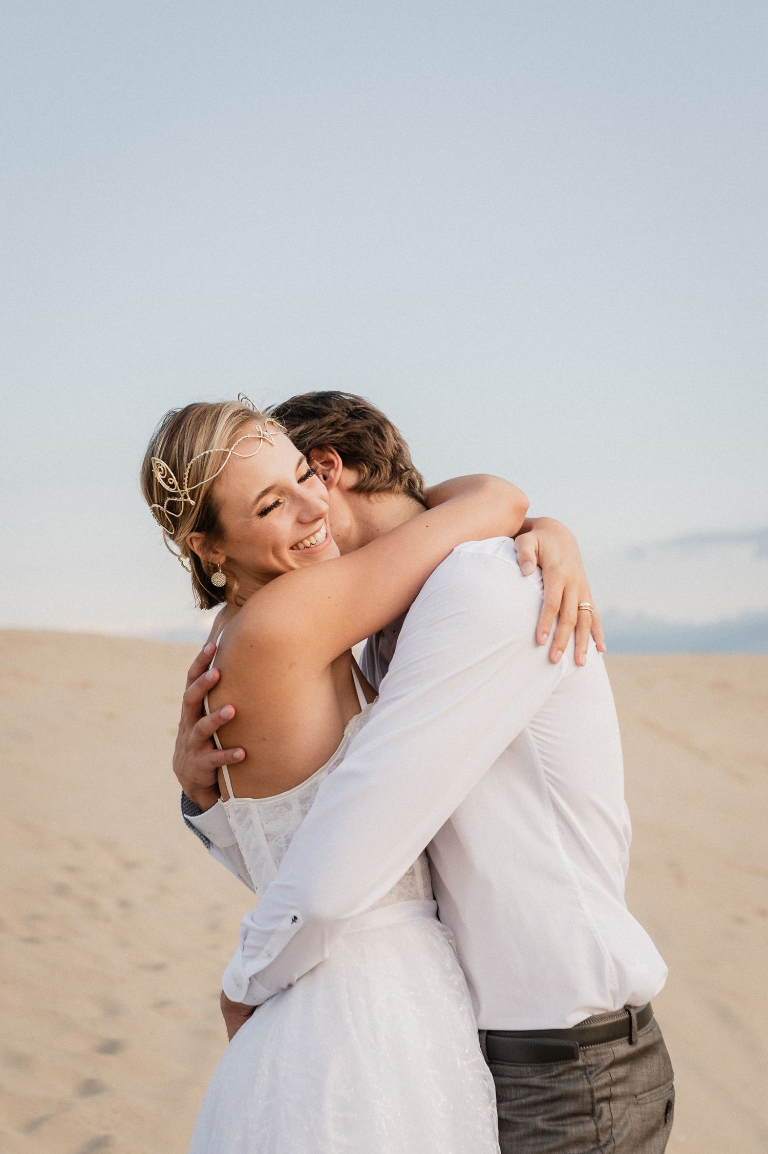 A couple embraces lovingly on a sandy beach during a romantic photo session.