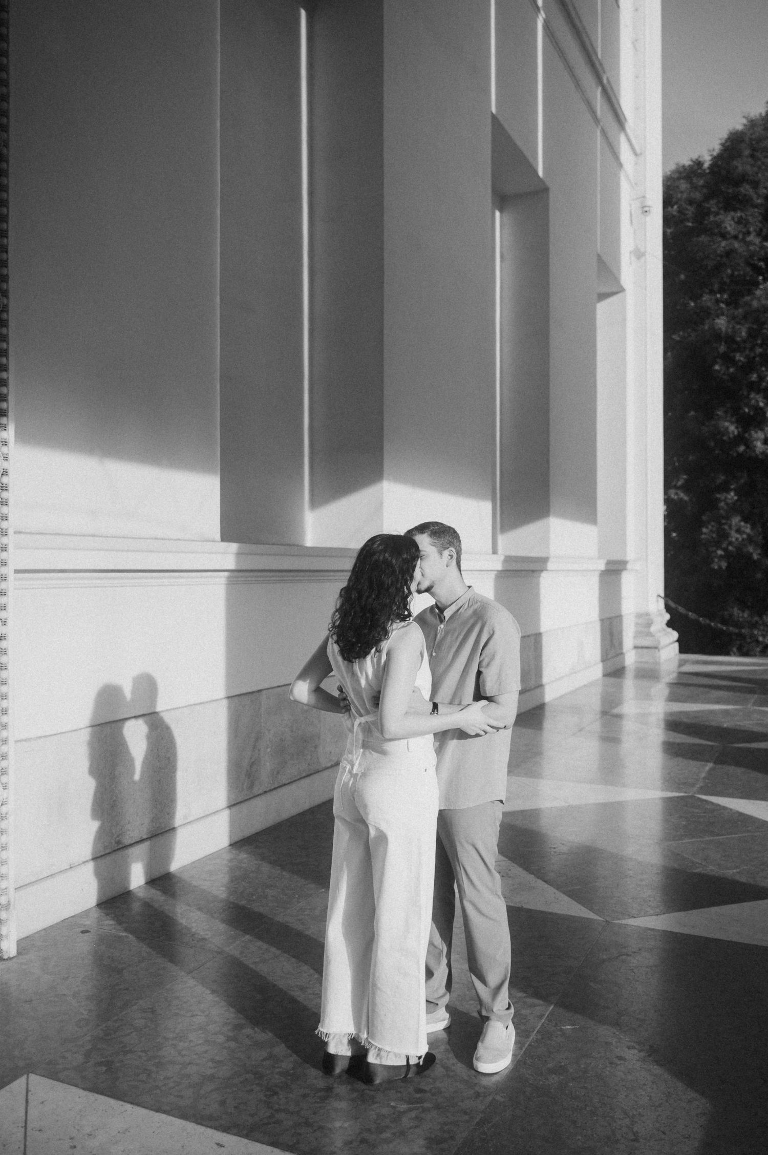 A romantic black and white portrait of a couple embracing near classical architecture.