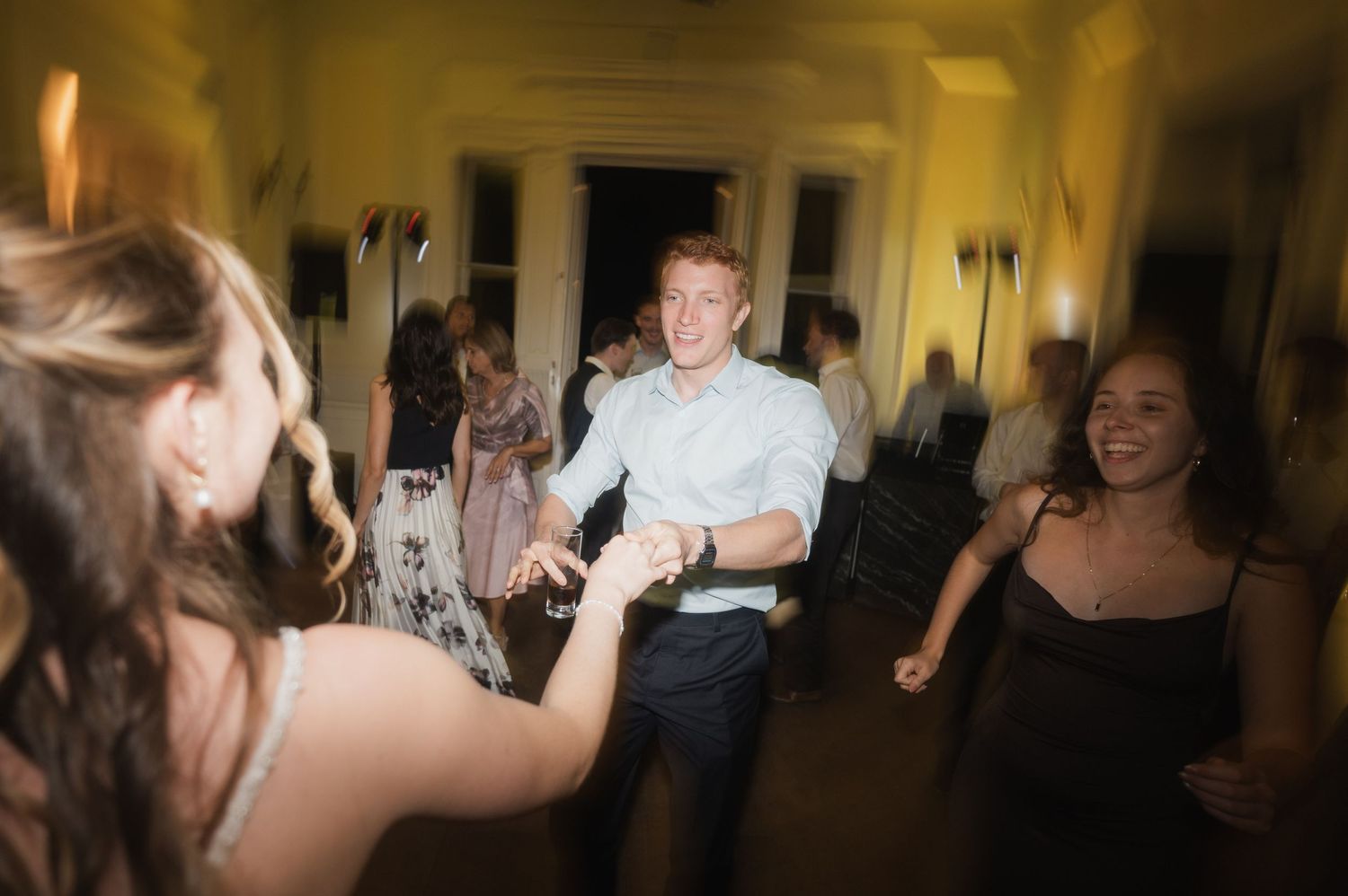 Wedding guests enjoy energetic dancing on warmly lit dance floor during lively reception party.