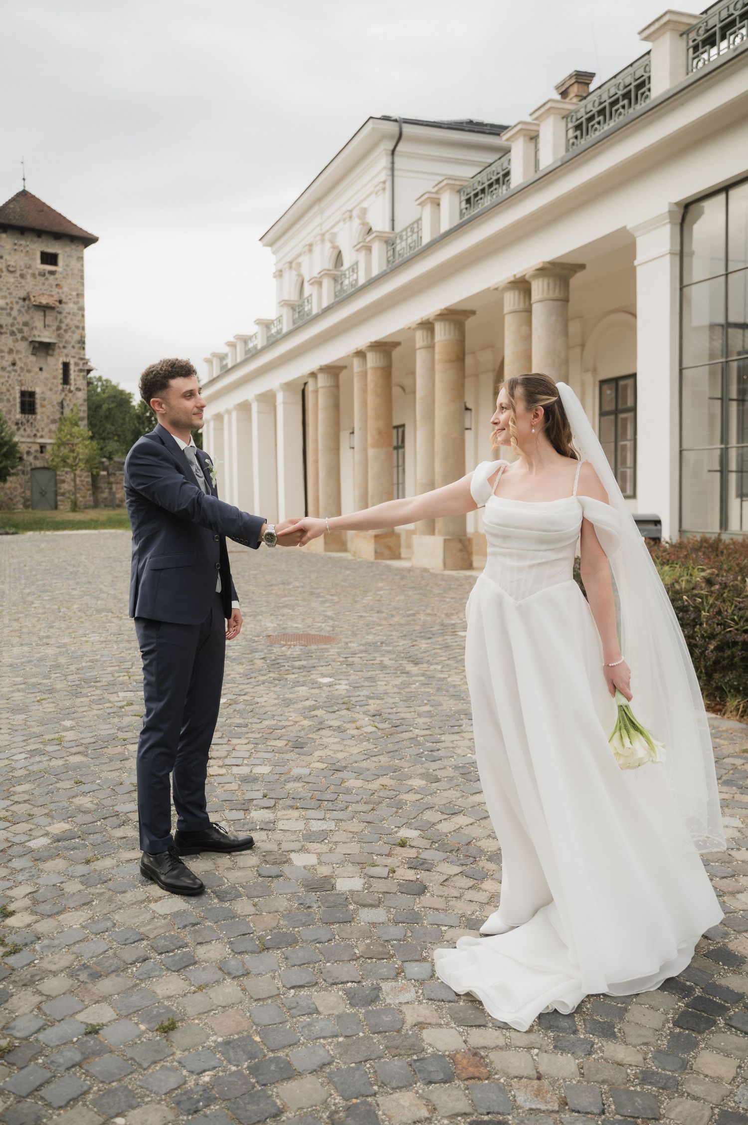 Bride and groom holding hands at arms length outside a grand white neoclassical wedding venue.