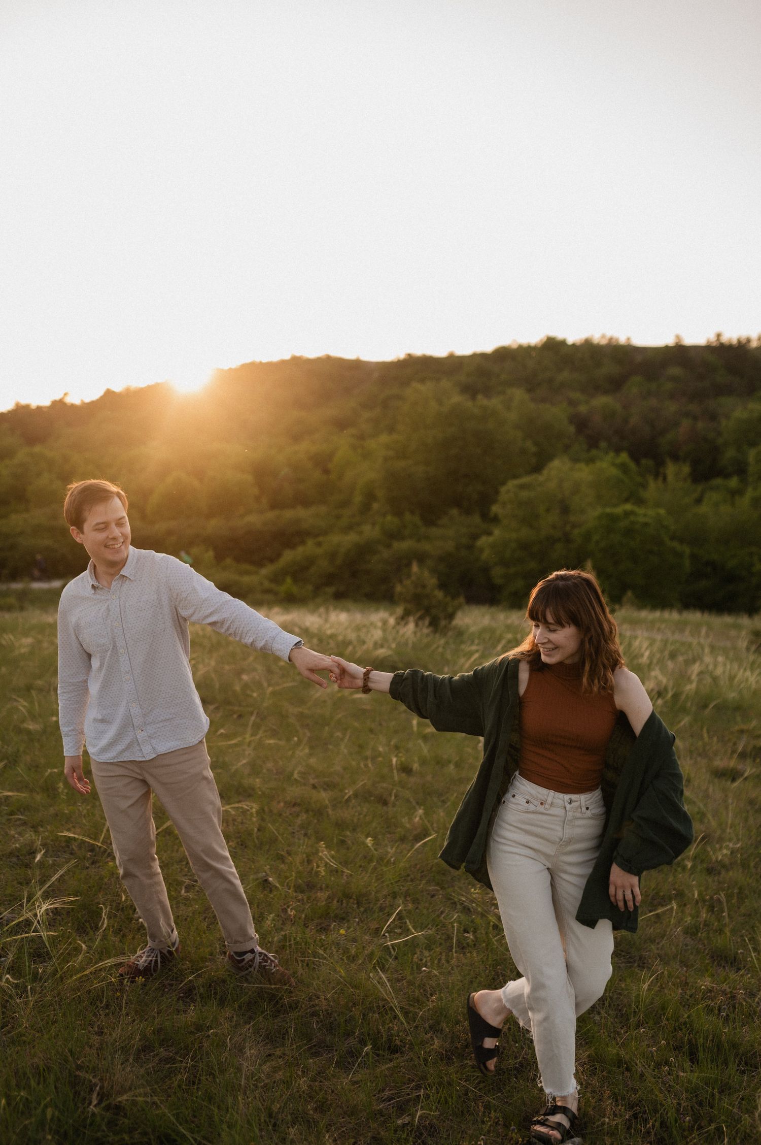 A playful couple dances and spins together in a sunlit field at golden hour.