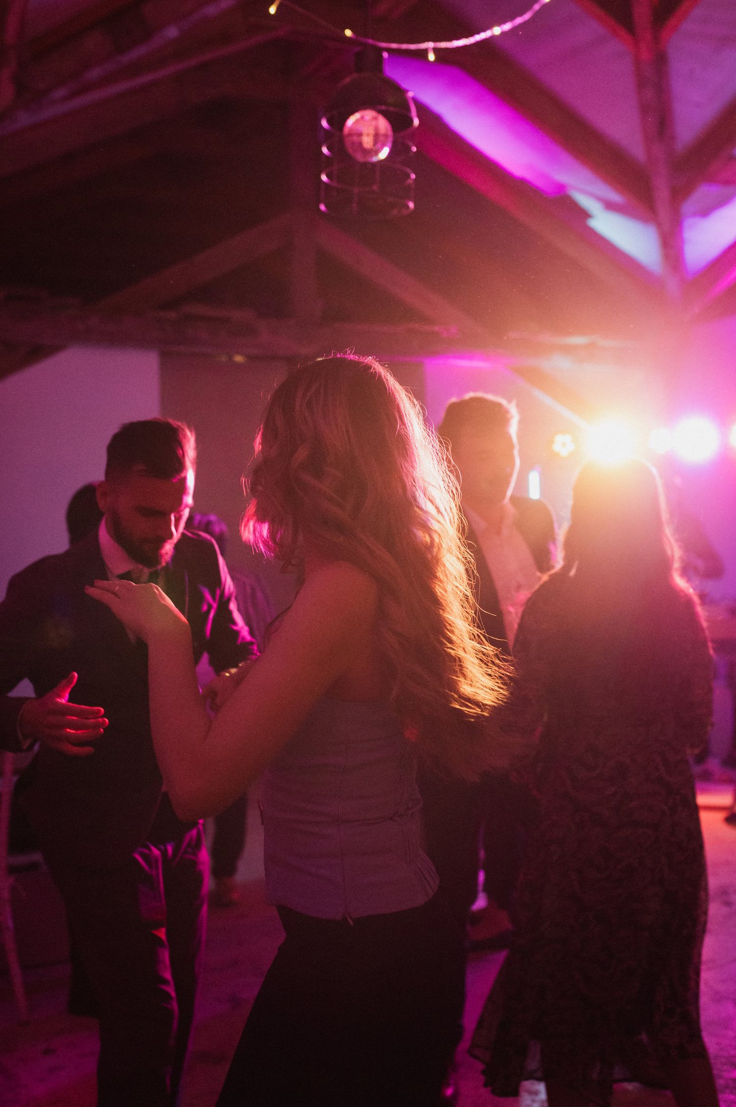 Silhouettes of couples dancing together in a dimly lit nightclub with pink and purple lighting effects.