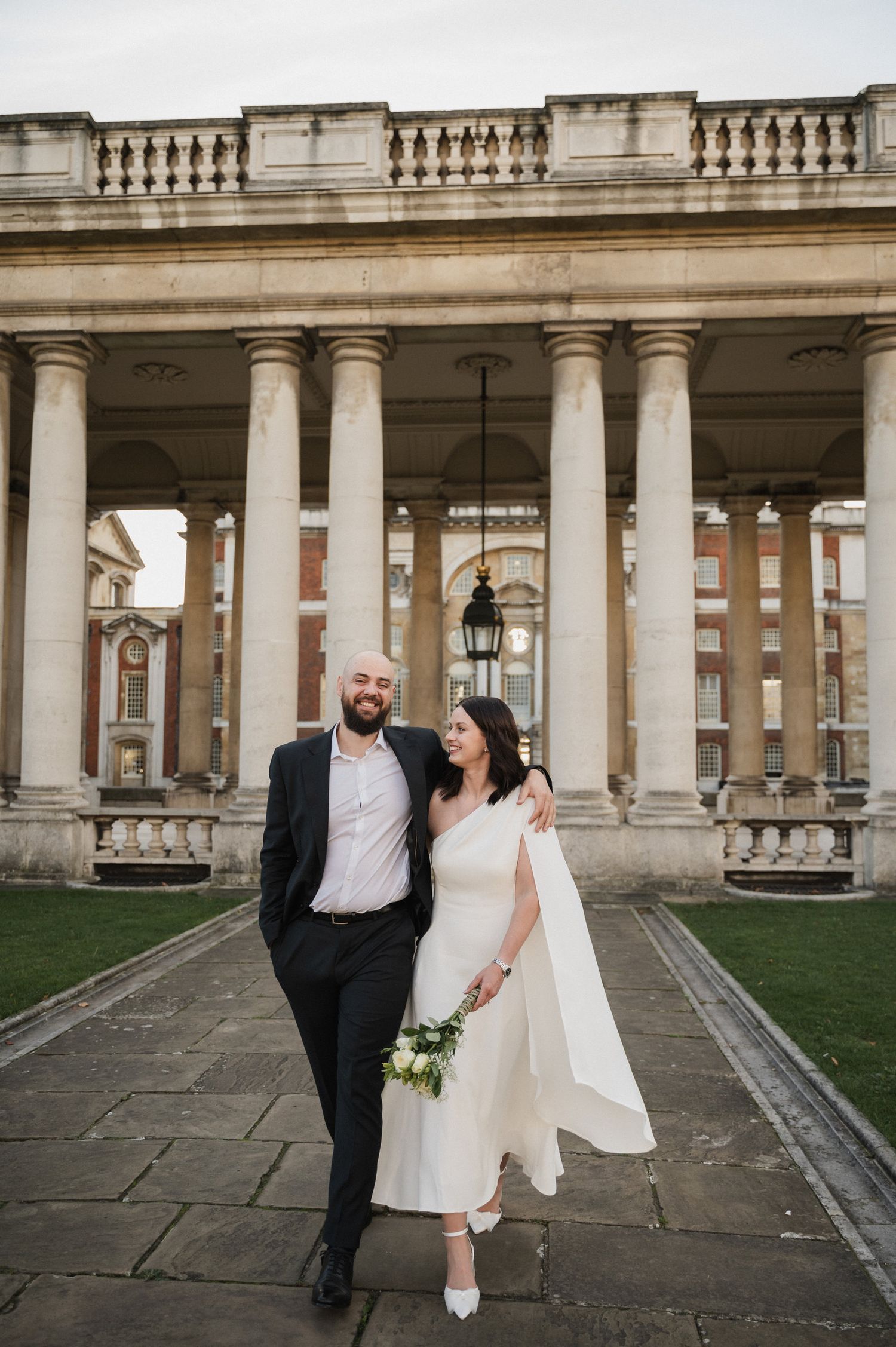 A couple poses amid majestic stone columns in an elegant outdoor setting.