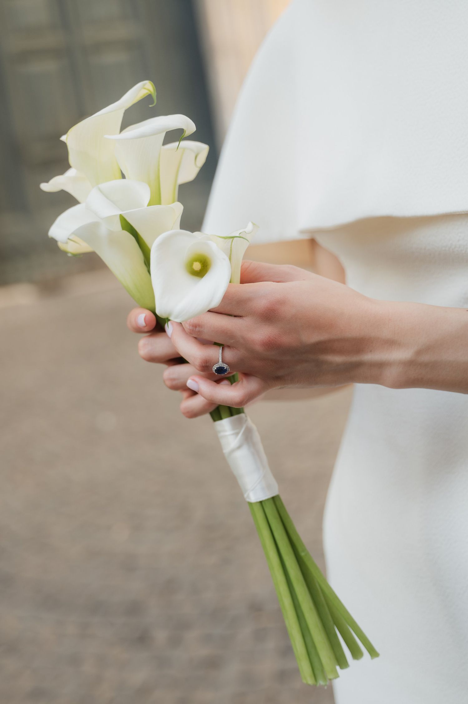Close-up shot of hands holding an elegant white calla lily wedding bouquet.