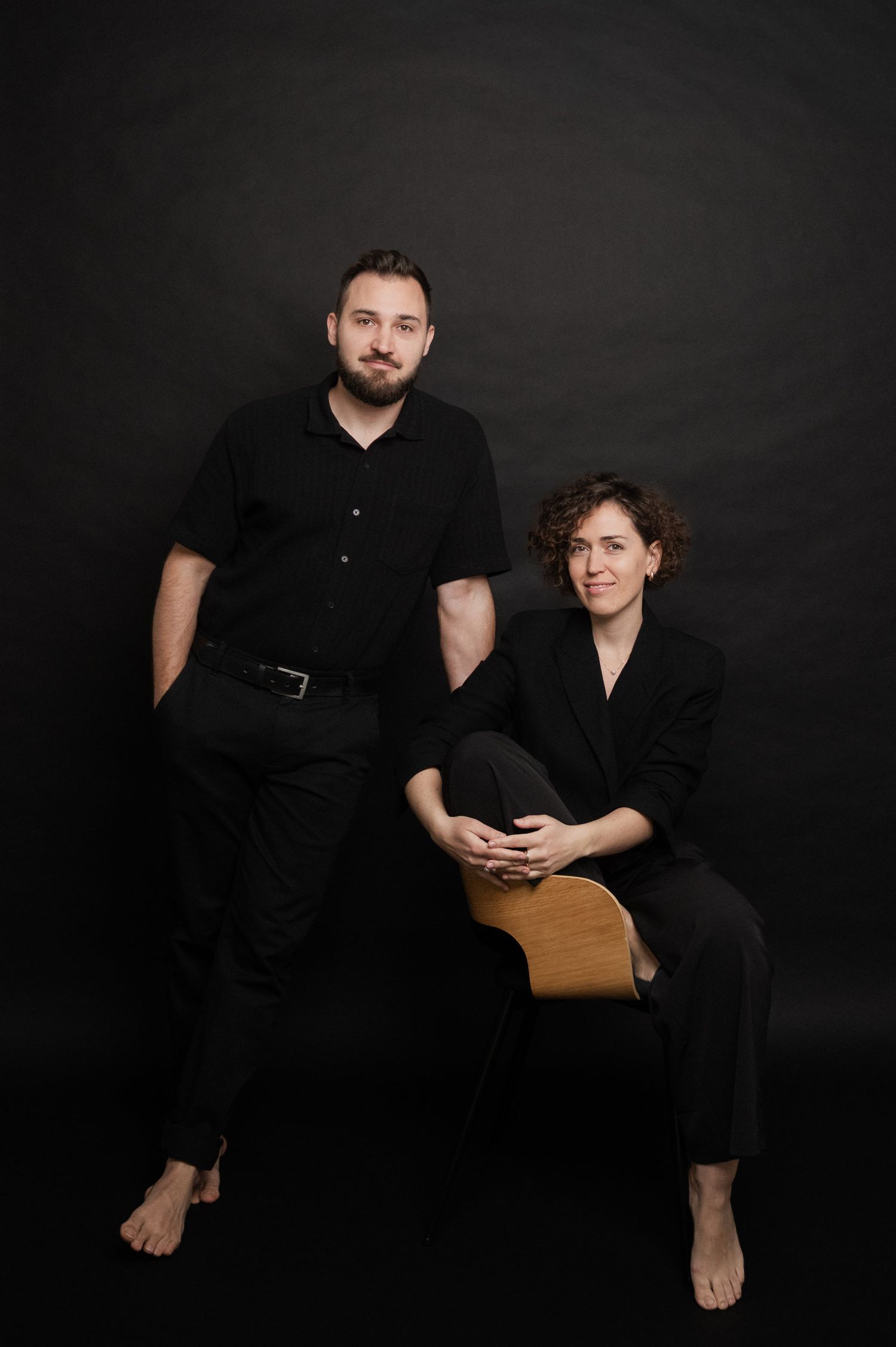 A black and white photo series showing two people in dark clothing sitting together against a dark background.