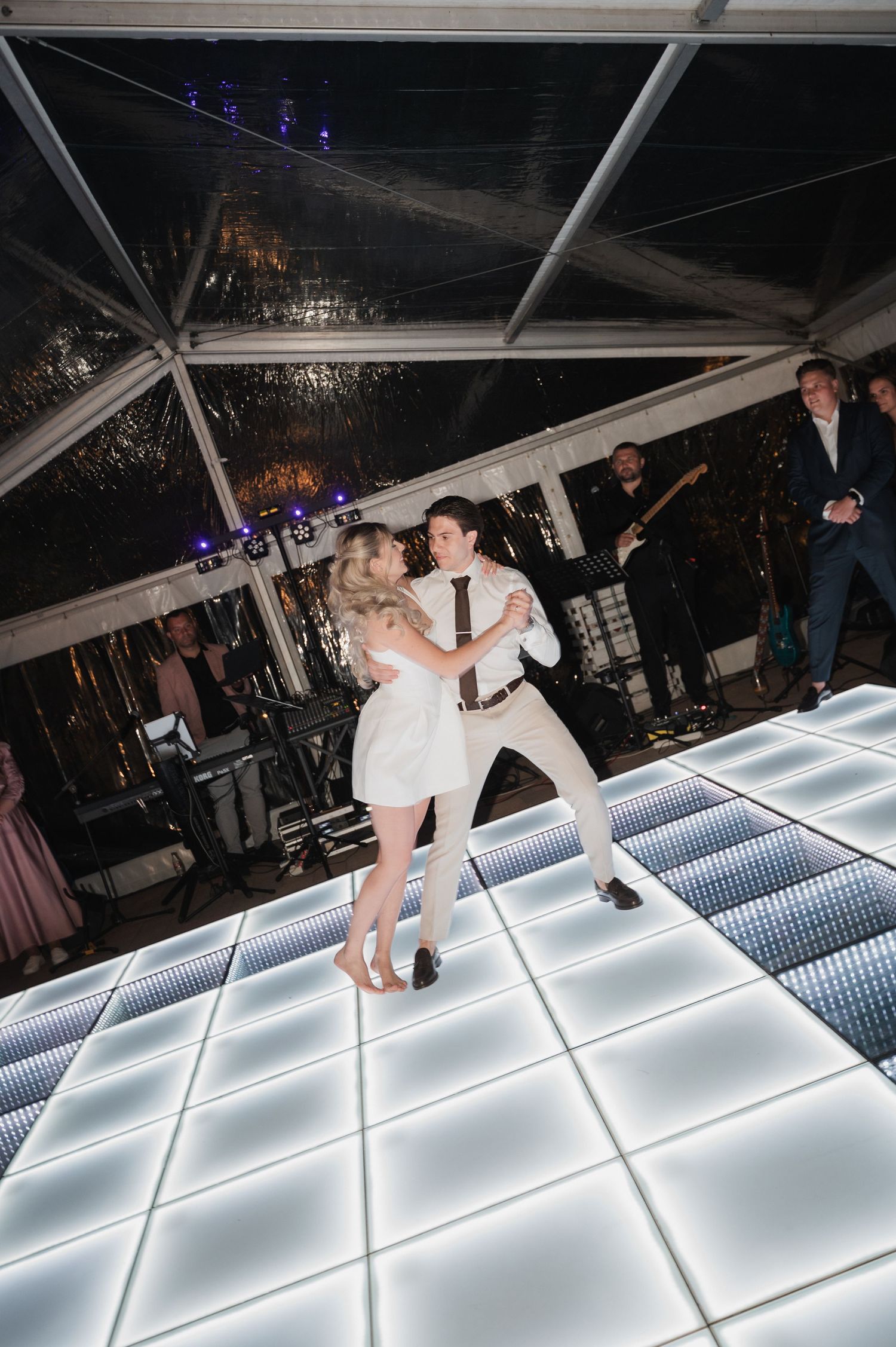Newlyweds sharing their first dance on a glowing LED dance floor under a clear wedding marquee.