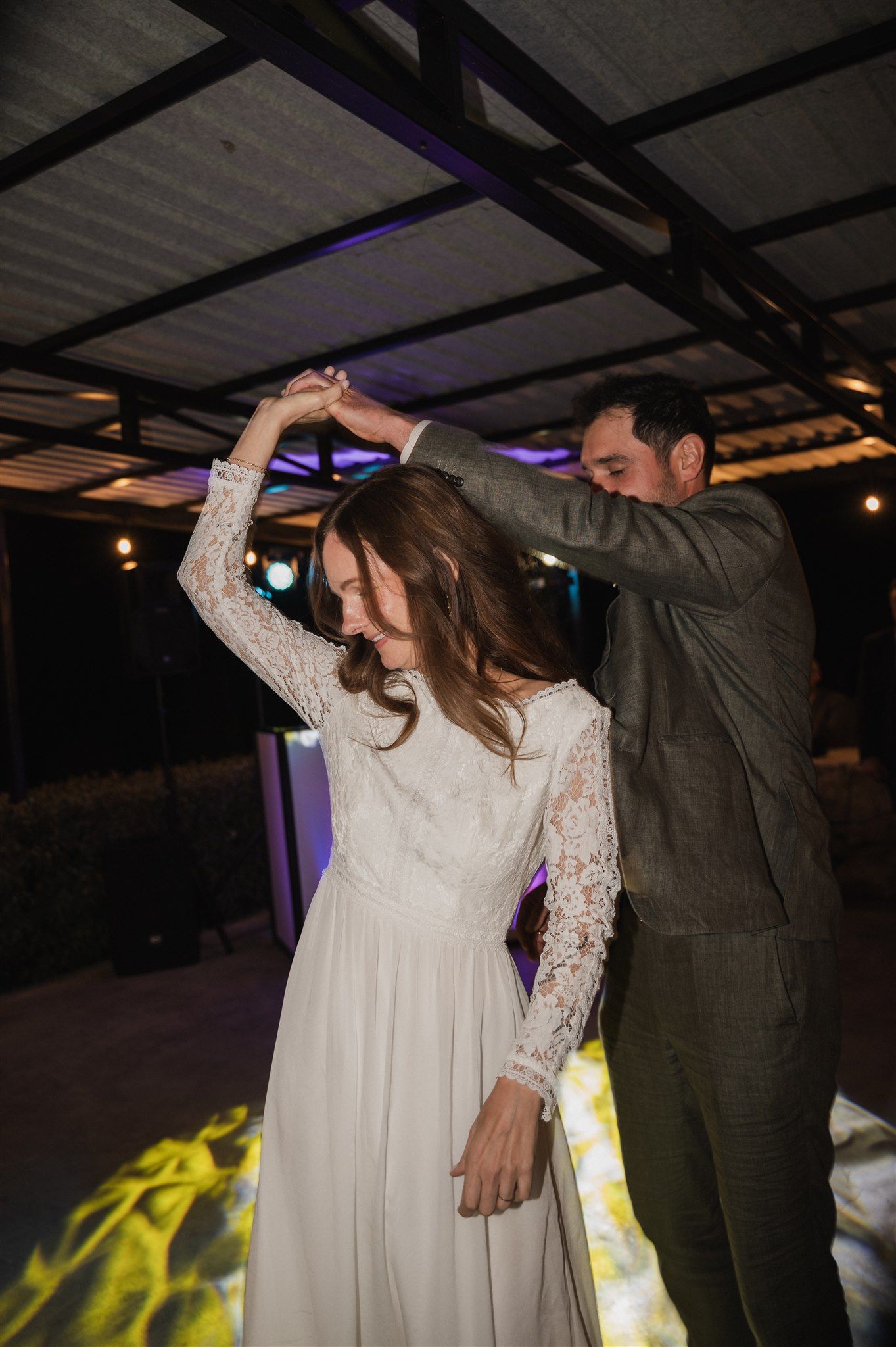 A couple dances together at a wedding reception with colorful lighting effects on the floor.