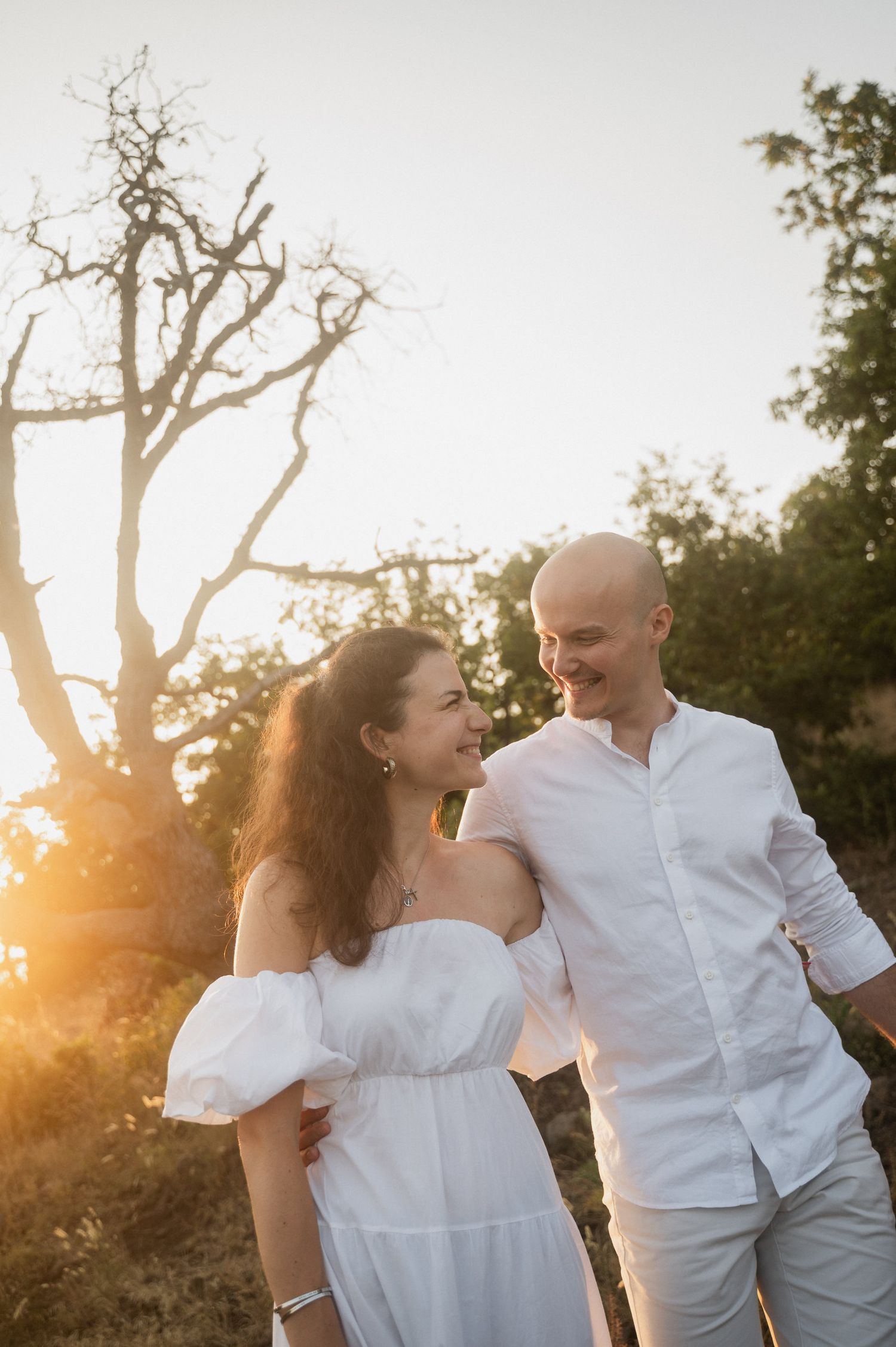 A couple shares joyful moments together during a sunset photoshoot in a natural outdoor setting.