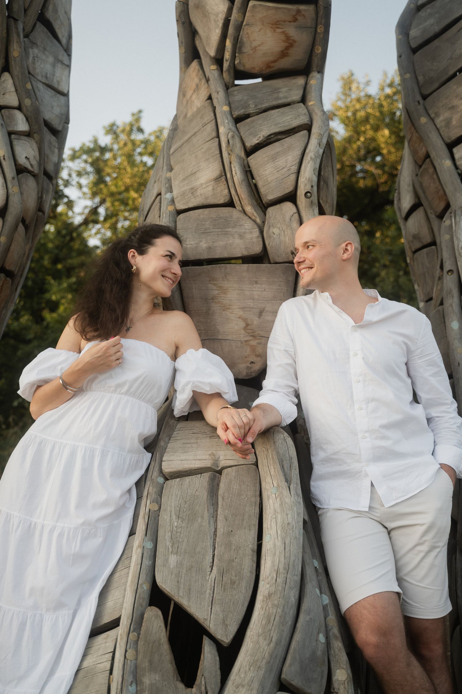 A series of four romantic photos showing a couple in white outfits posing playfully against a rustic wooden wall outdoors.