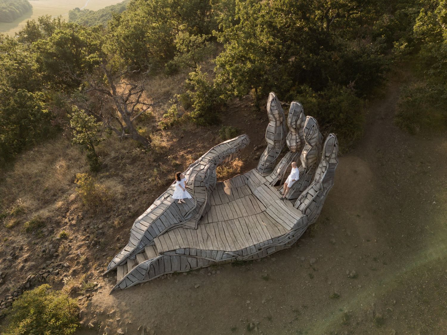 A large outdoor art installation of a reclining figure made from curved wooden slats creates a sculptural form in nature.