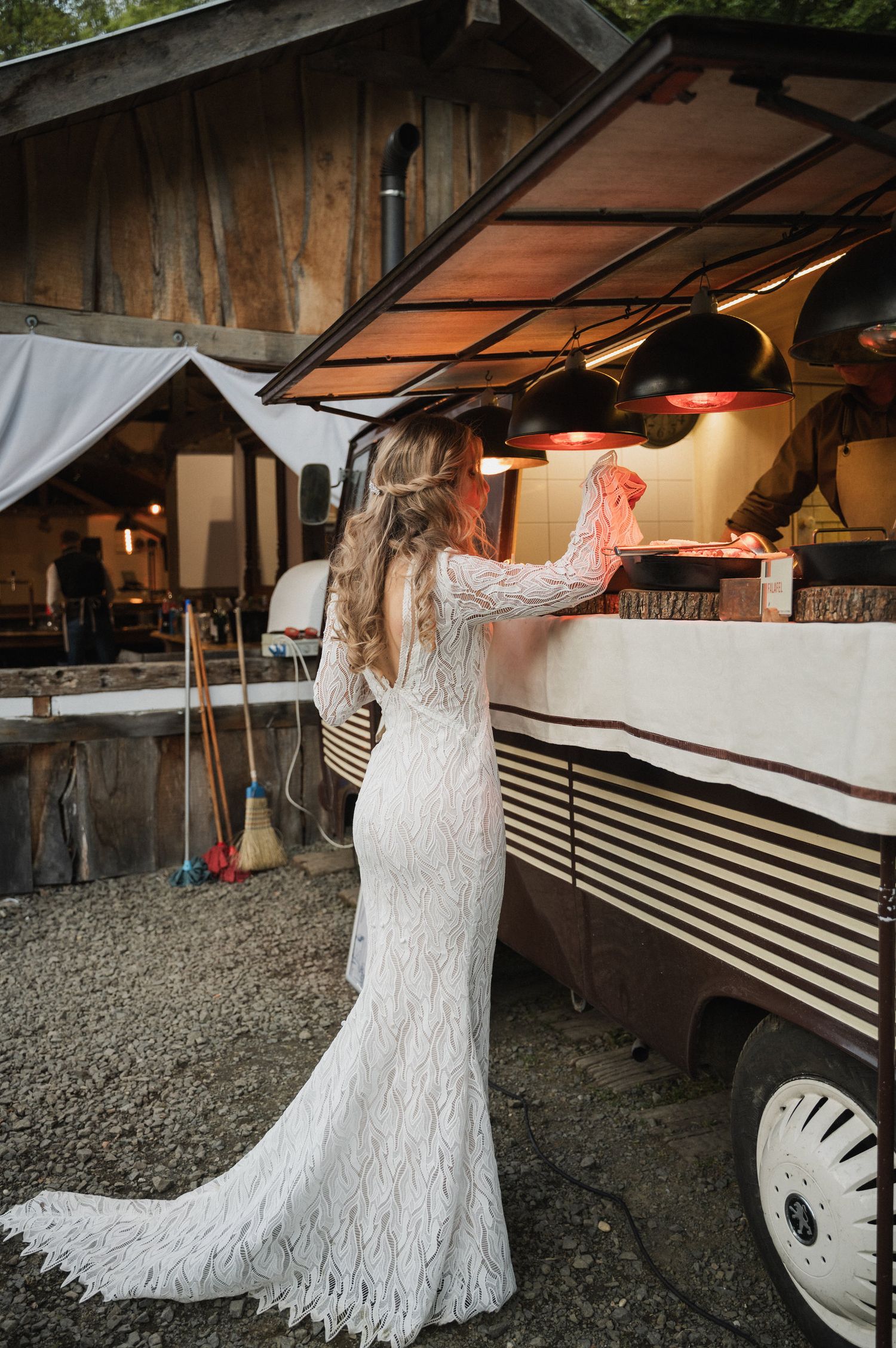 A bride in a lace wedding dress twirls and dances under a covered outdoor venue.