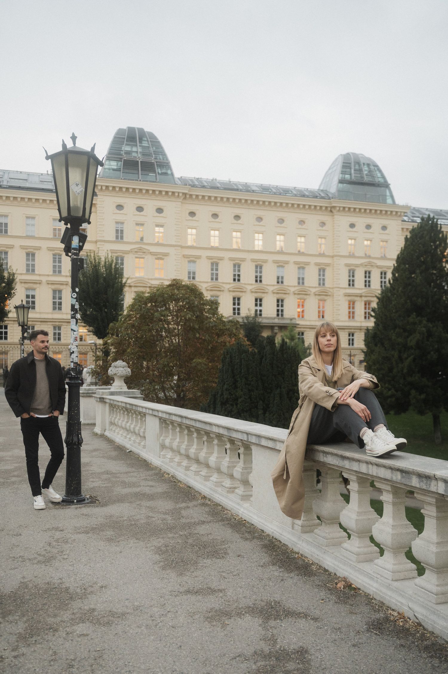 Two people posing near ornate stone balustrade with historic domed building in background in Vienna, Austria.