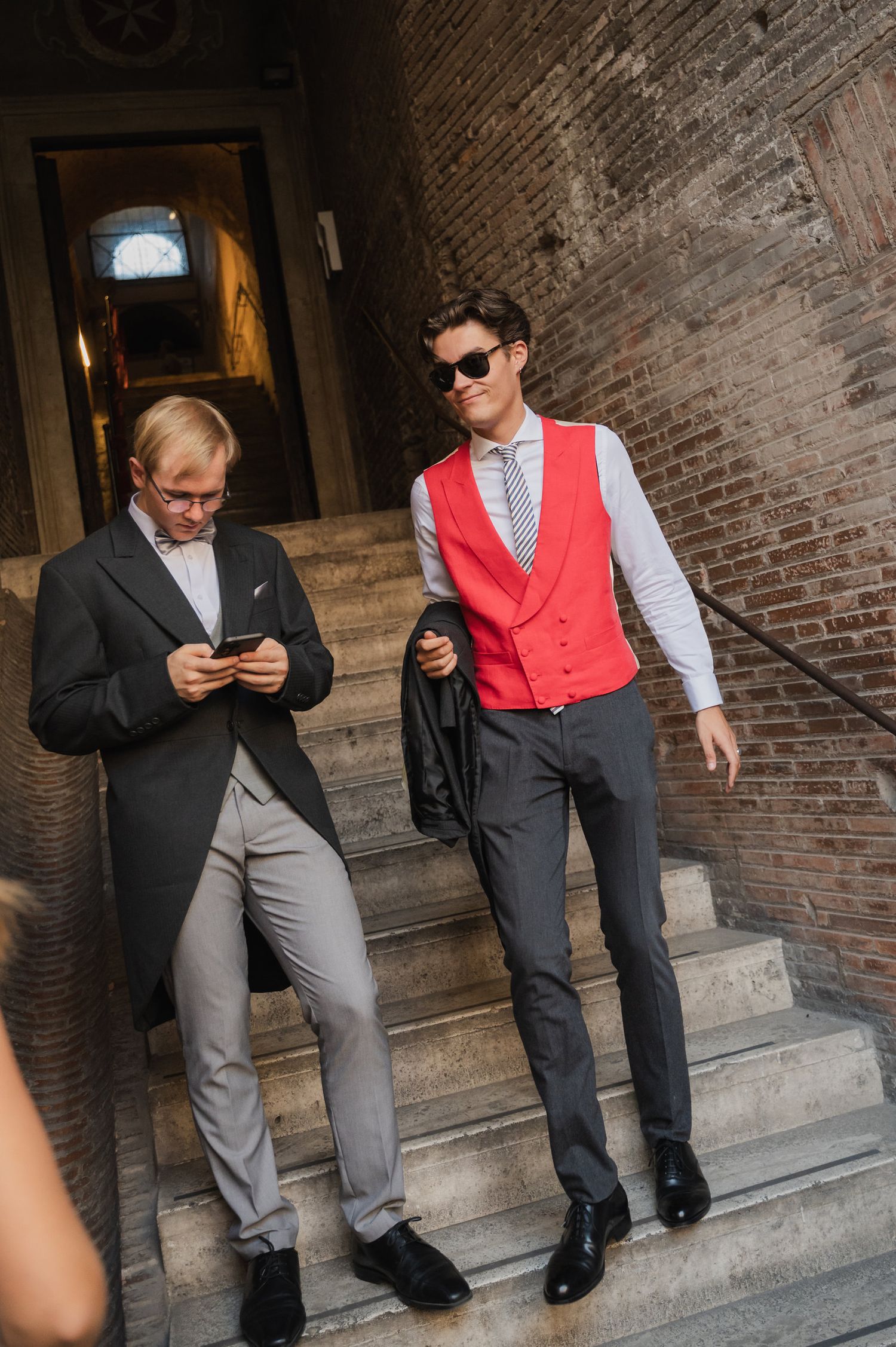 Wedding party members in formal attire standing on stone steps of historic building.
