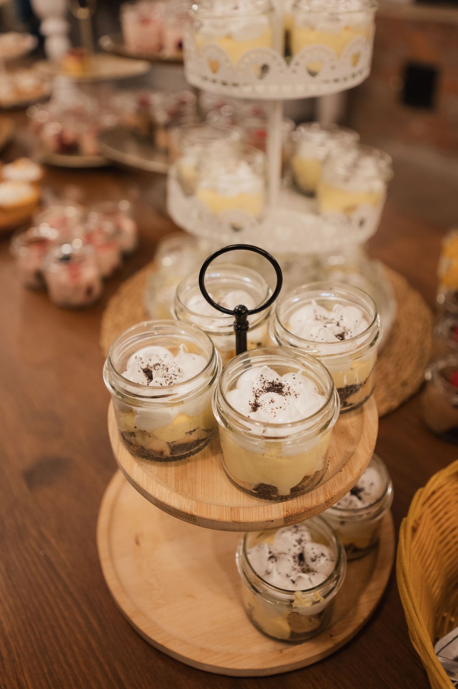 Elegant dessert display featuring tiramisu in mason jars arranged on a wooden tiered stand at a wedding.