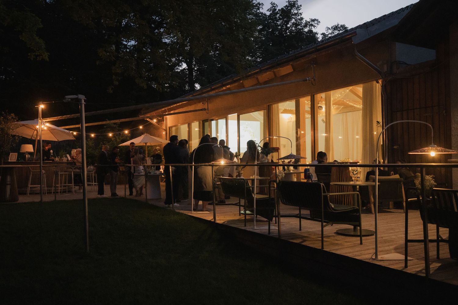Warmly lit wedding venue patio at night with string lights and guests mingling outdoors.