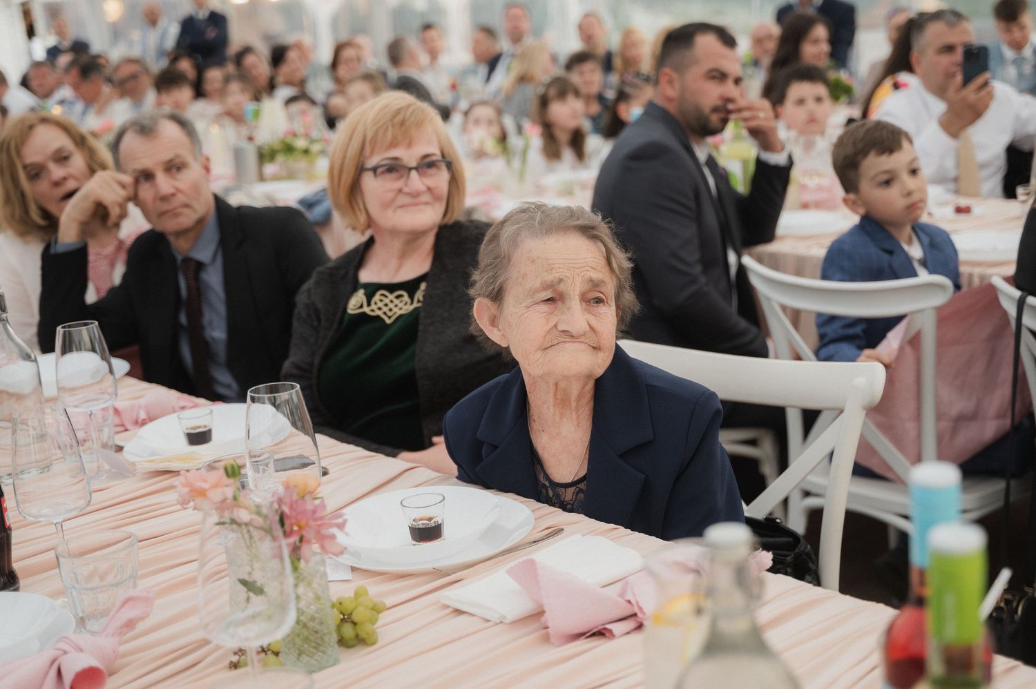 Elderly wedding guest seated at a decorated reception table surrounded by family members during a wedding celebration.