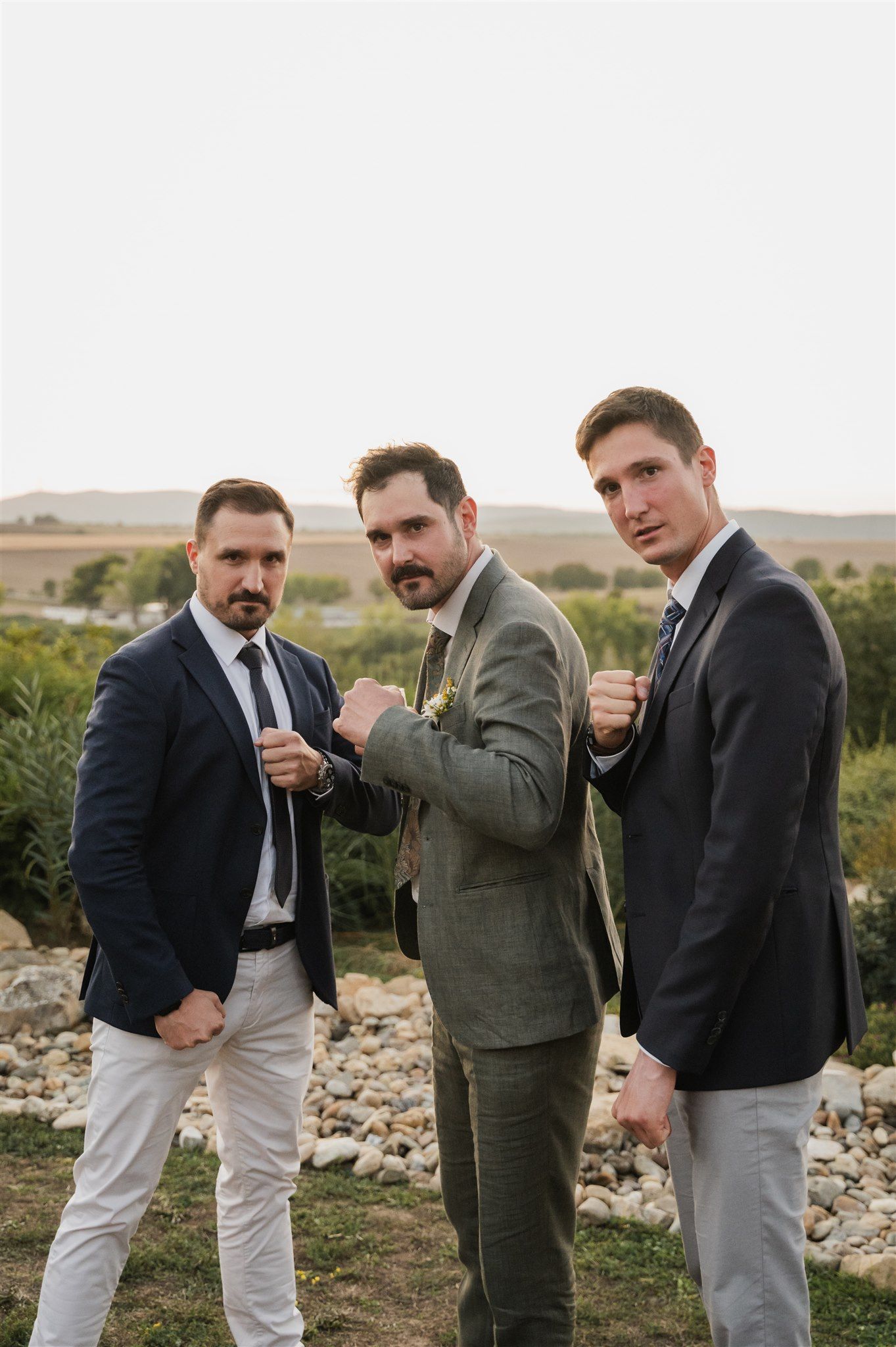 Groomsmen in suits posing together outdoors for wedding photos.