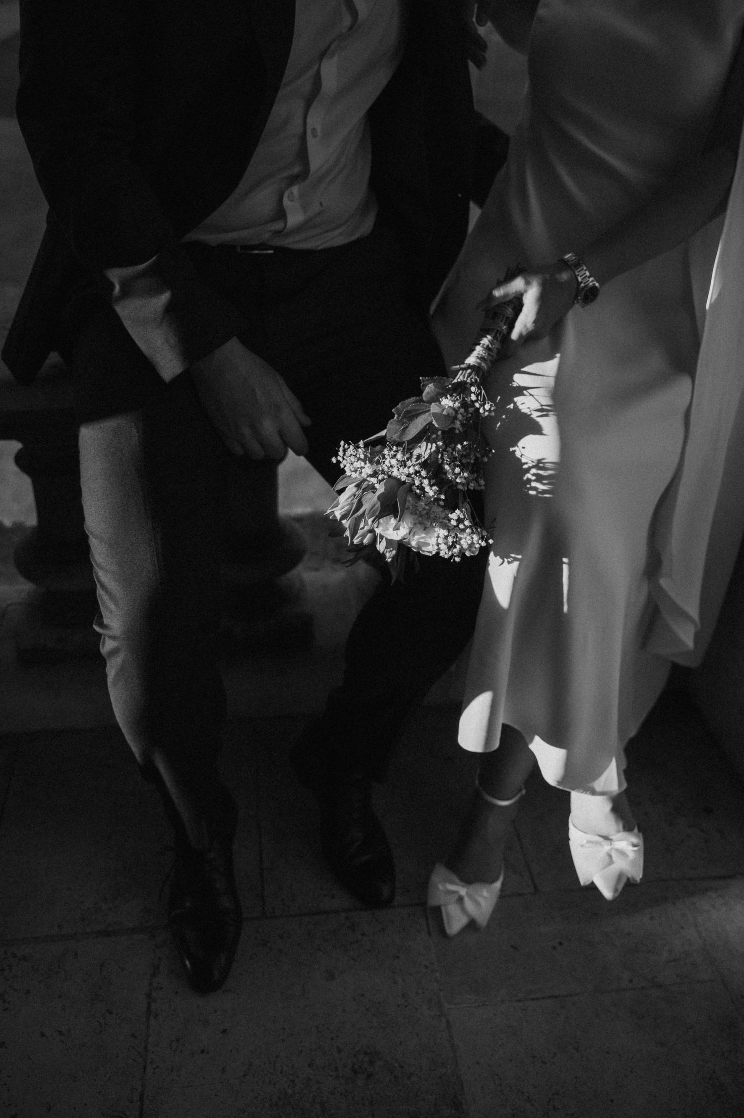 Black and white detail shot of formal shoes and dress hem on stone pavement.