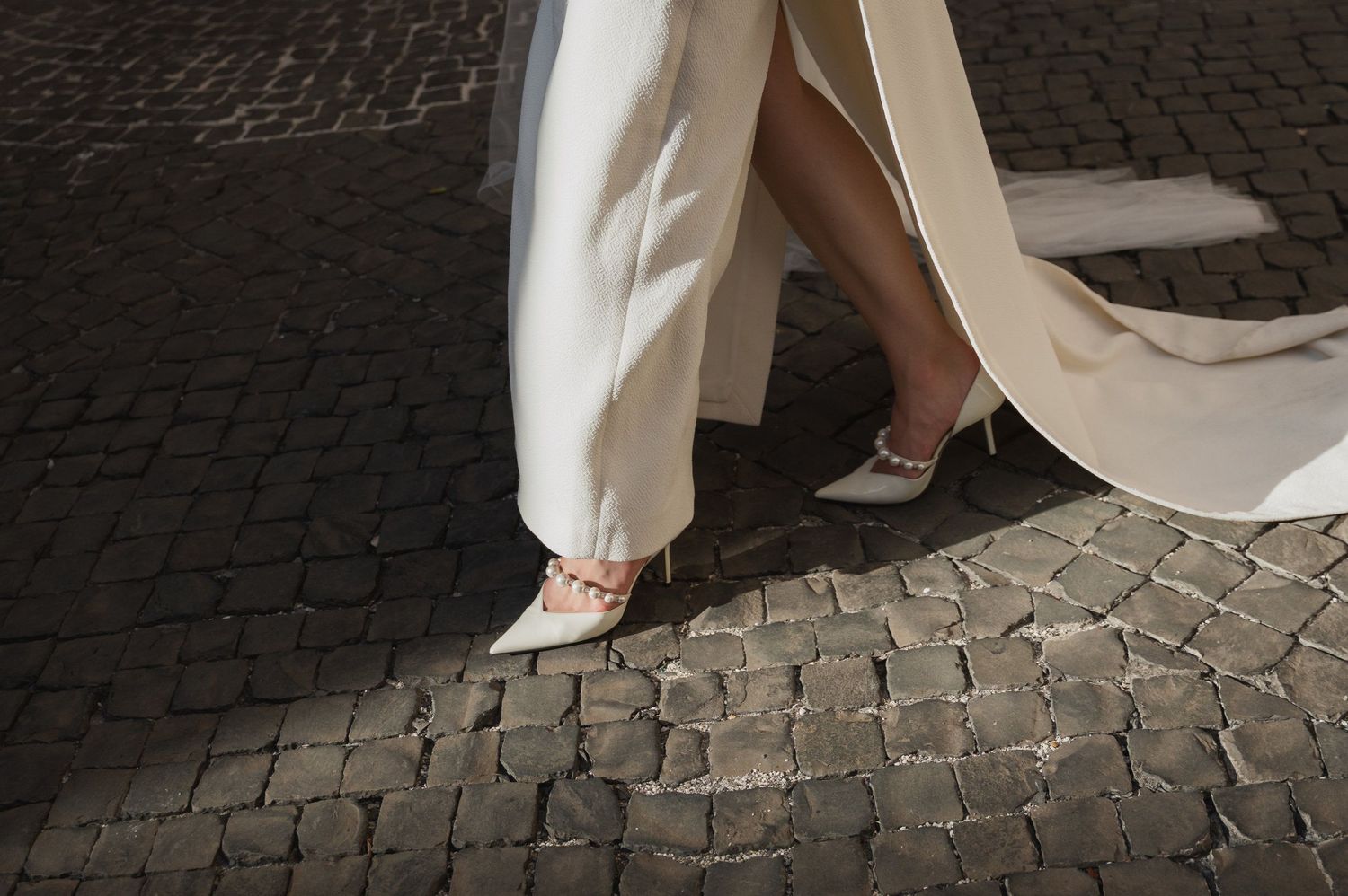 Elegant white wedding dress flowing over ancient cobblestone pavement.