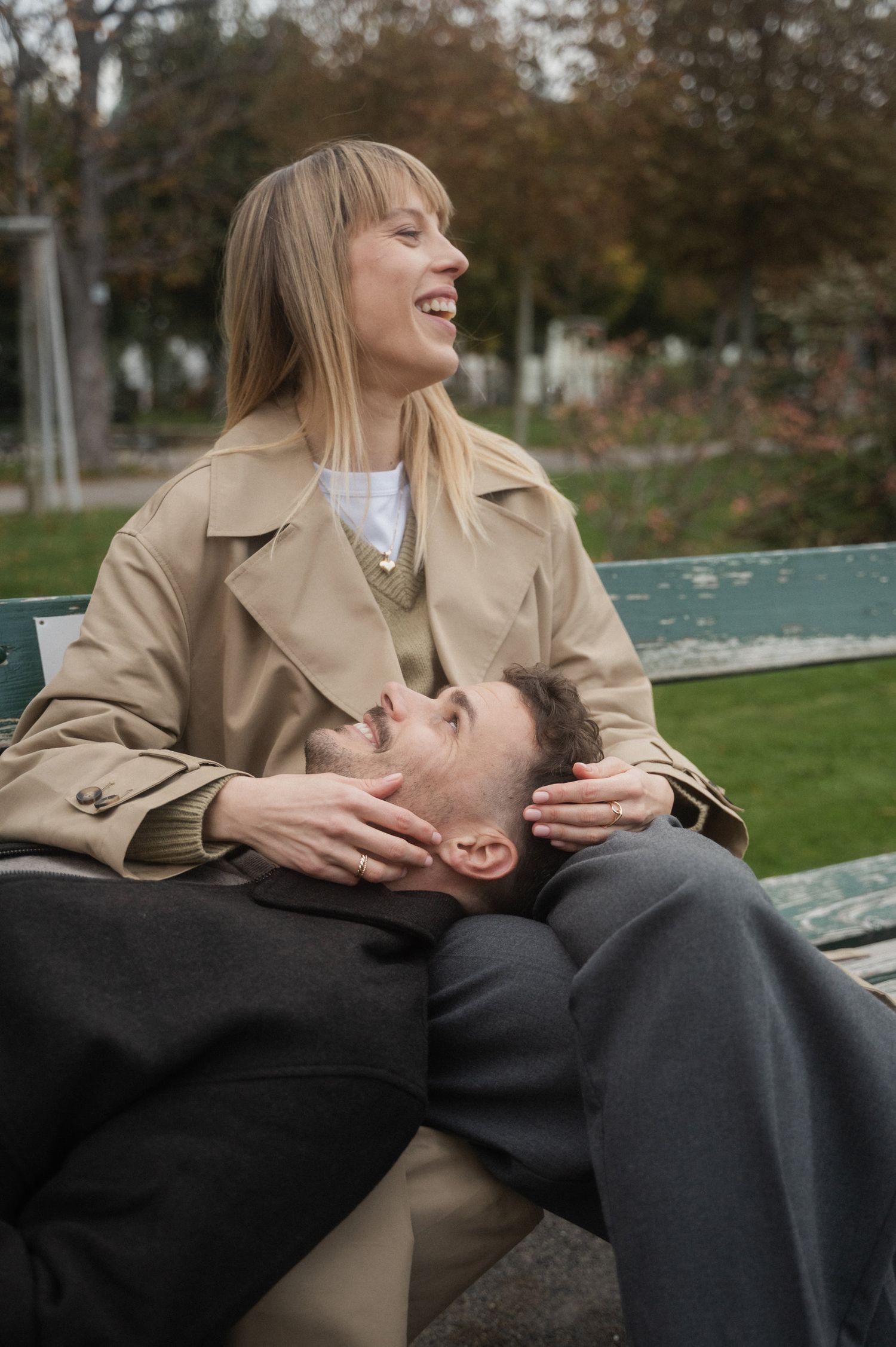 A couple shares a tender moment on a park bench as they laugh together on an autumn day.