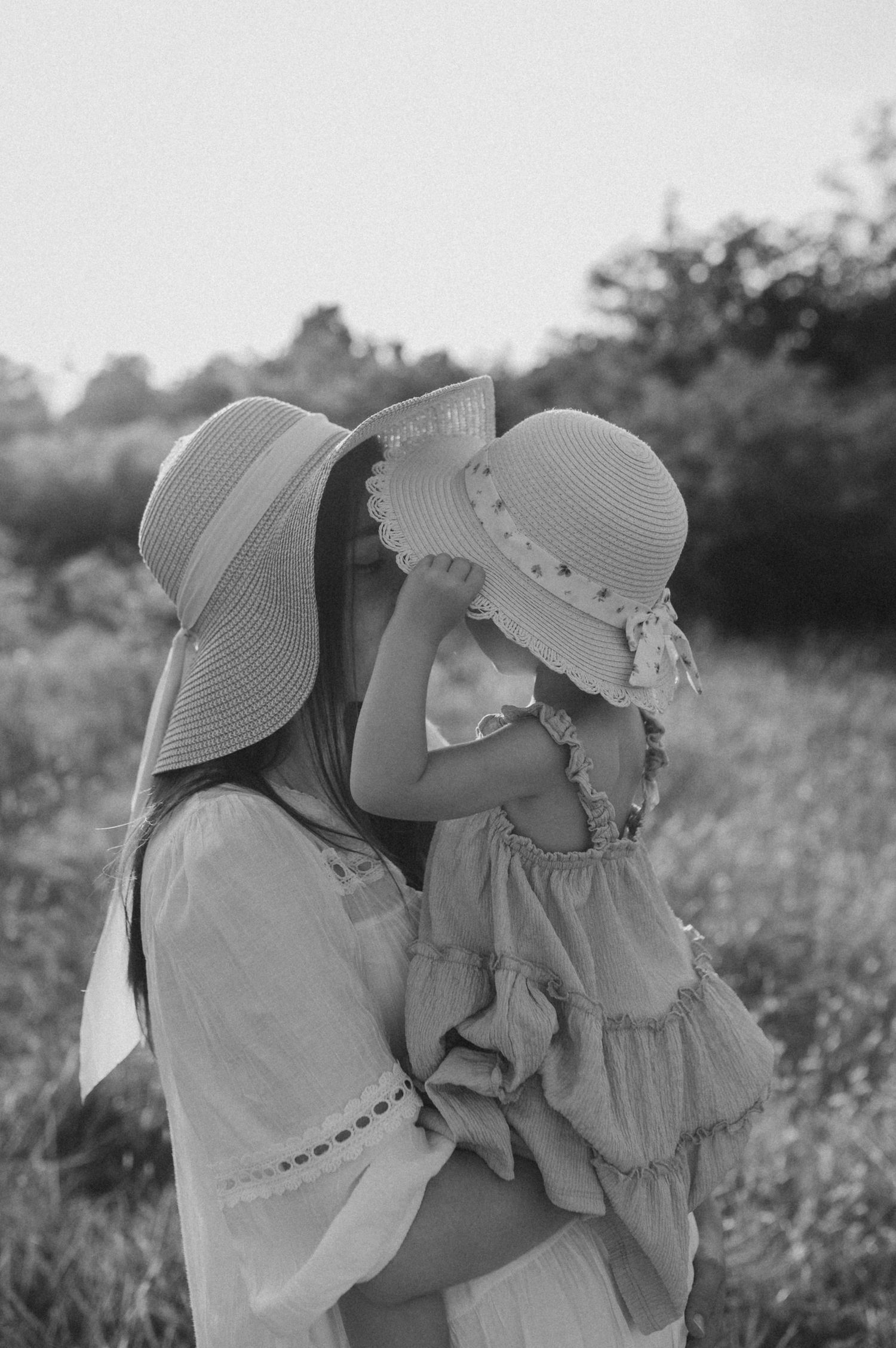 A black and white photo series shows two people in sun hats sharing tender moments in a field.