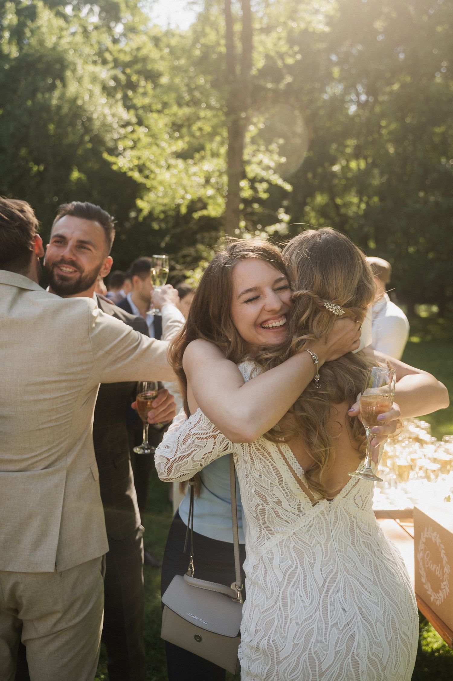Wedding guests share joyful embraces and celebrate during an outdoor reception in golden sunlight.