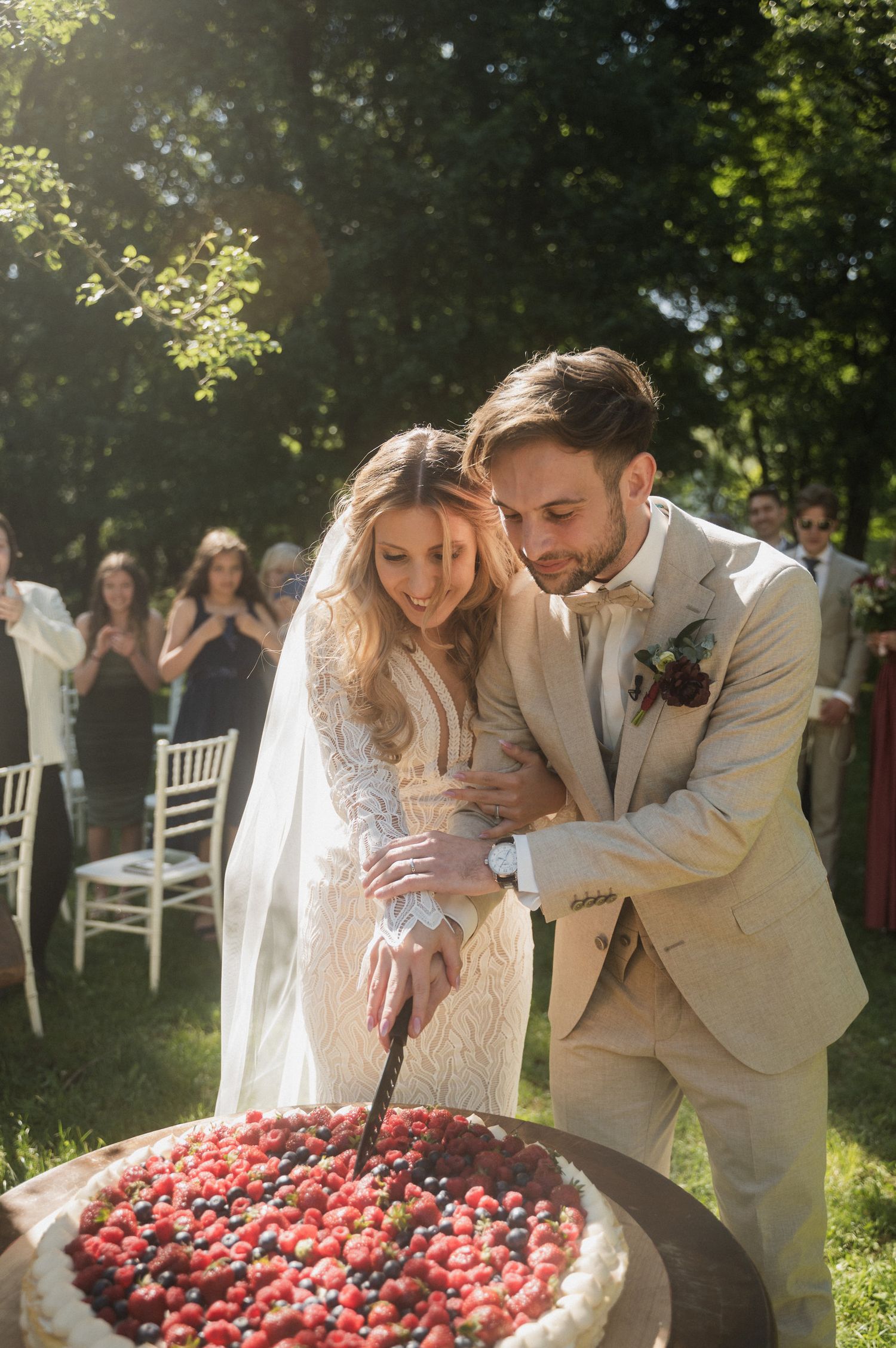 A couple shares a romantic moment beside a heart made of red rose petals in a sunny garden setting.