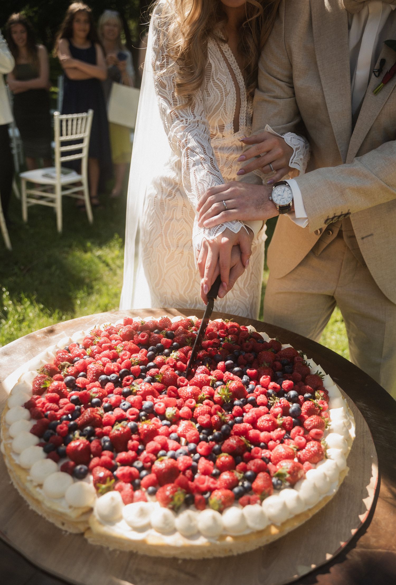 A large round pavlova dessert topped with fresh berries and whipped cream being served at an outdoor celebration.