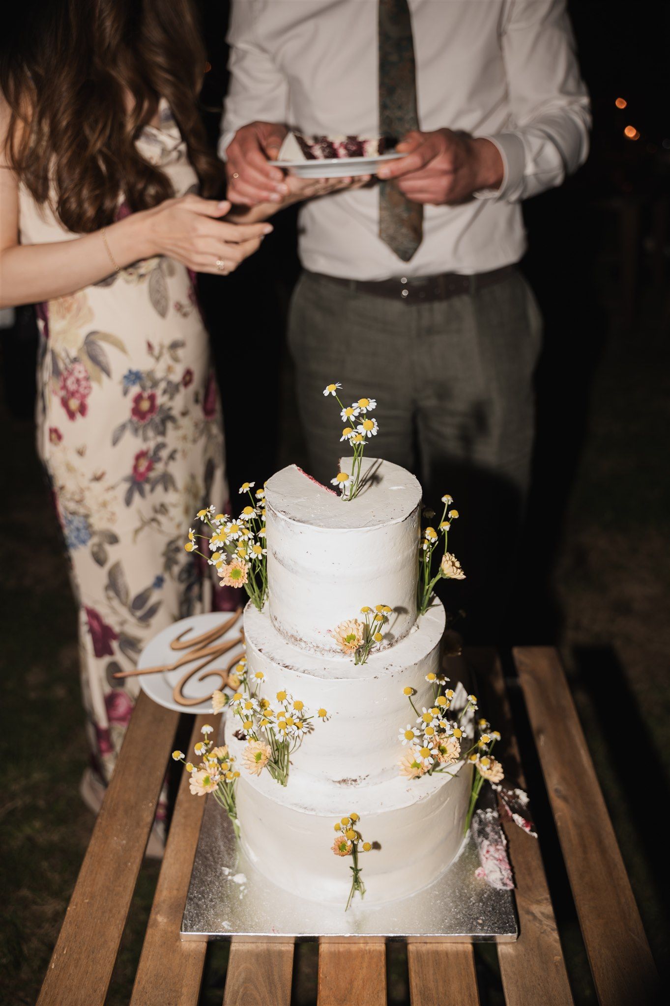 White tiered wedding cake adorned with small yellow flowers displayed on wooden table.