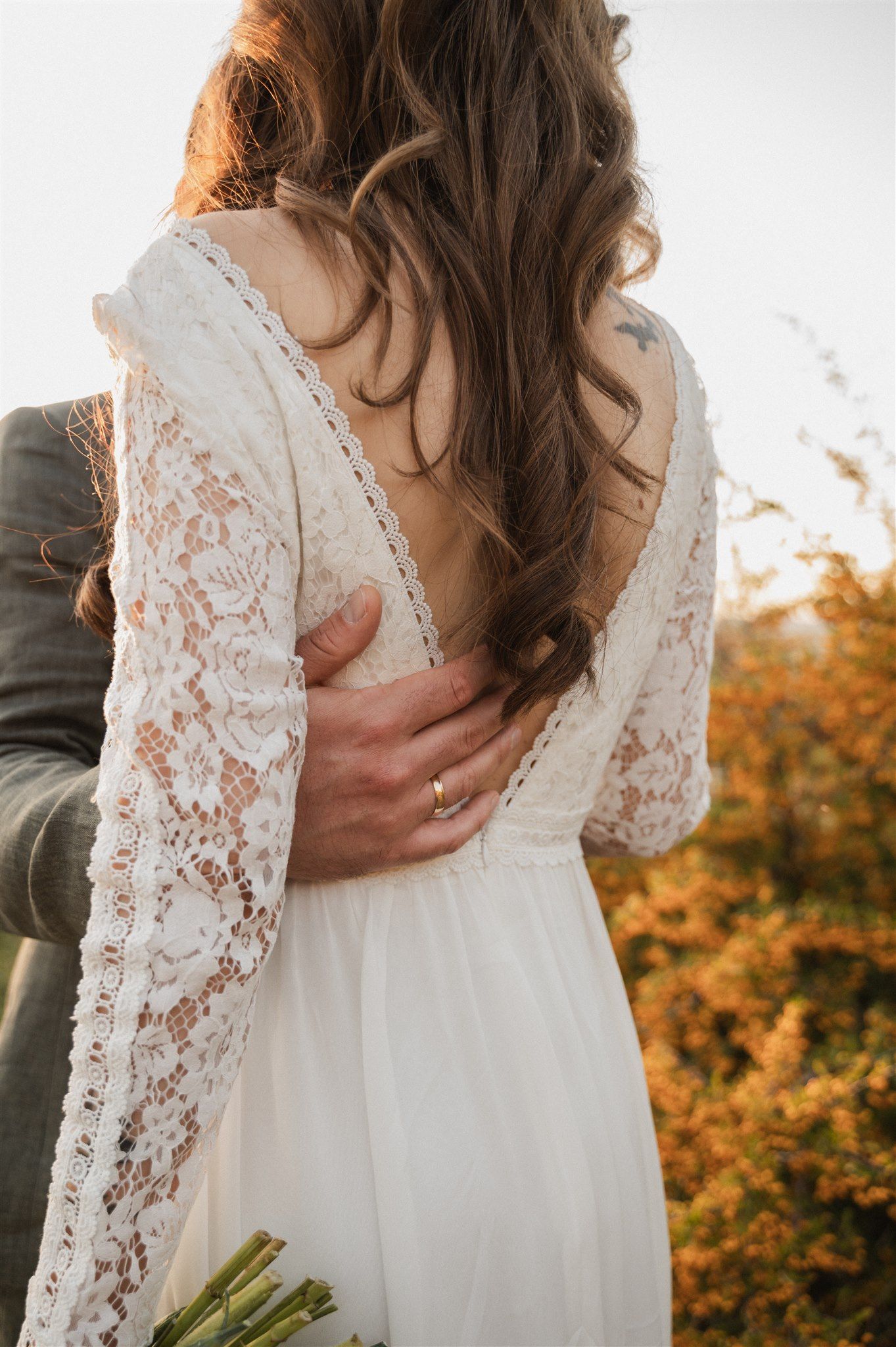 Intimate wedding moment showing lace sleeve dress detail and romantic embrace during golden hour.