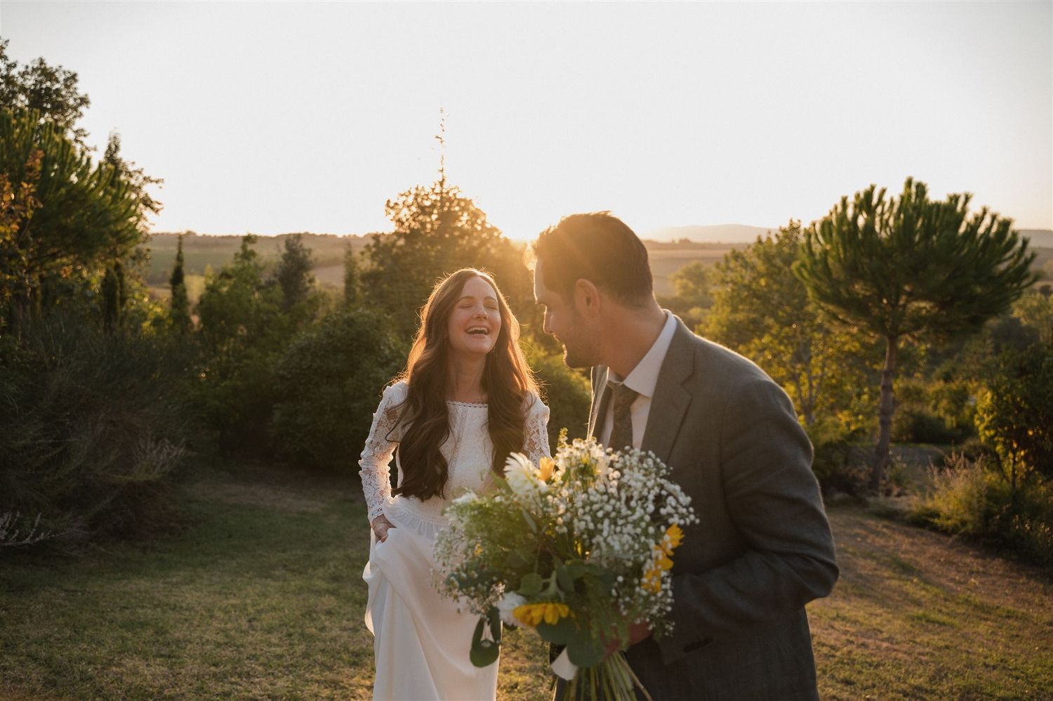 Wedding couple embracing in a golden field at sunset with wildflowers.