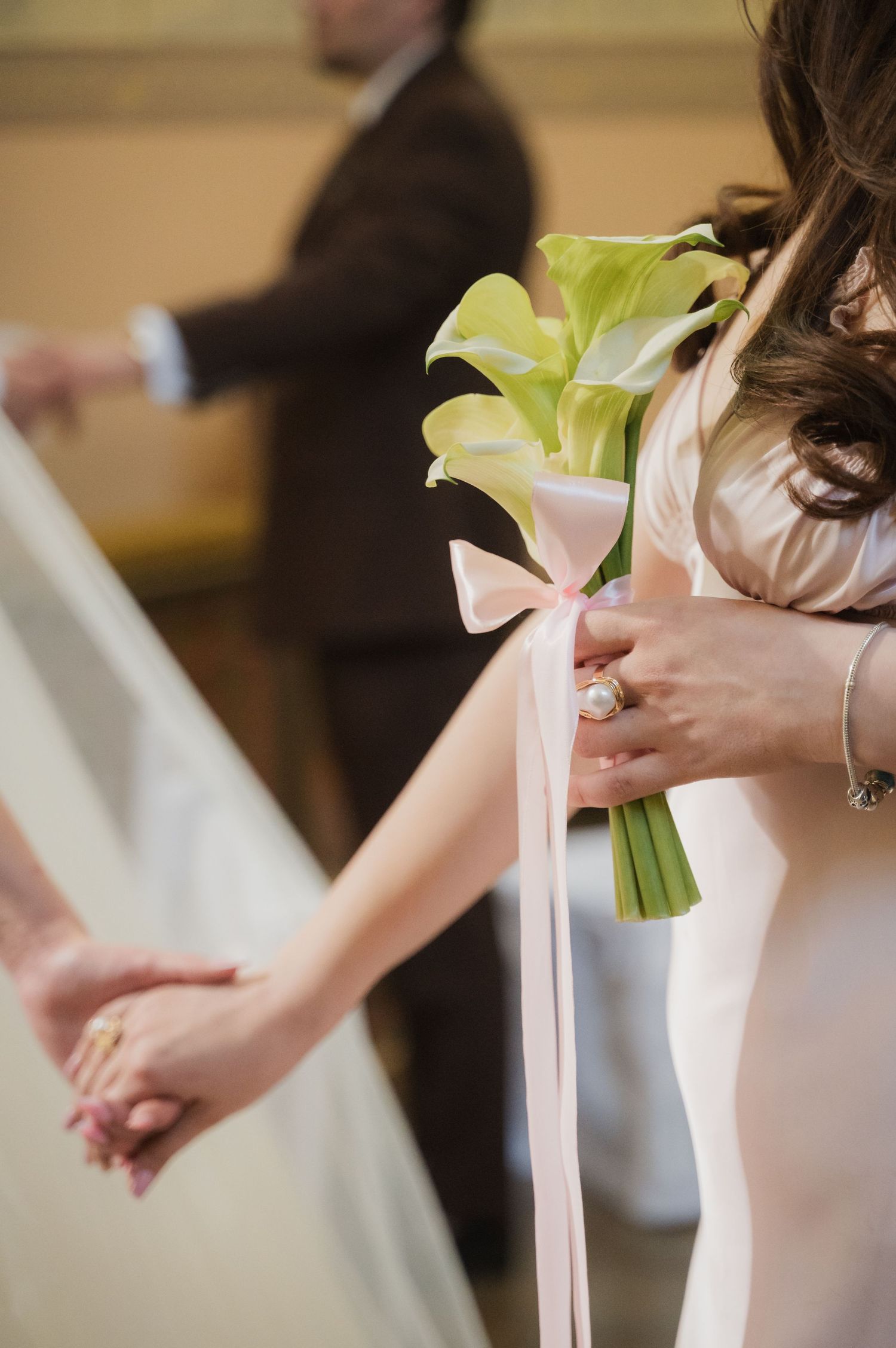 Bridesmaid holds green calla lily bouquet tied with pink ribbon during wedding ceremony.