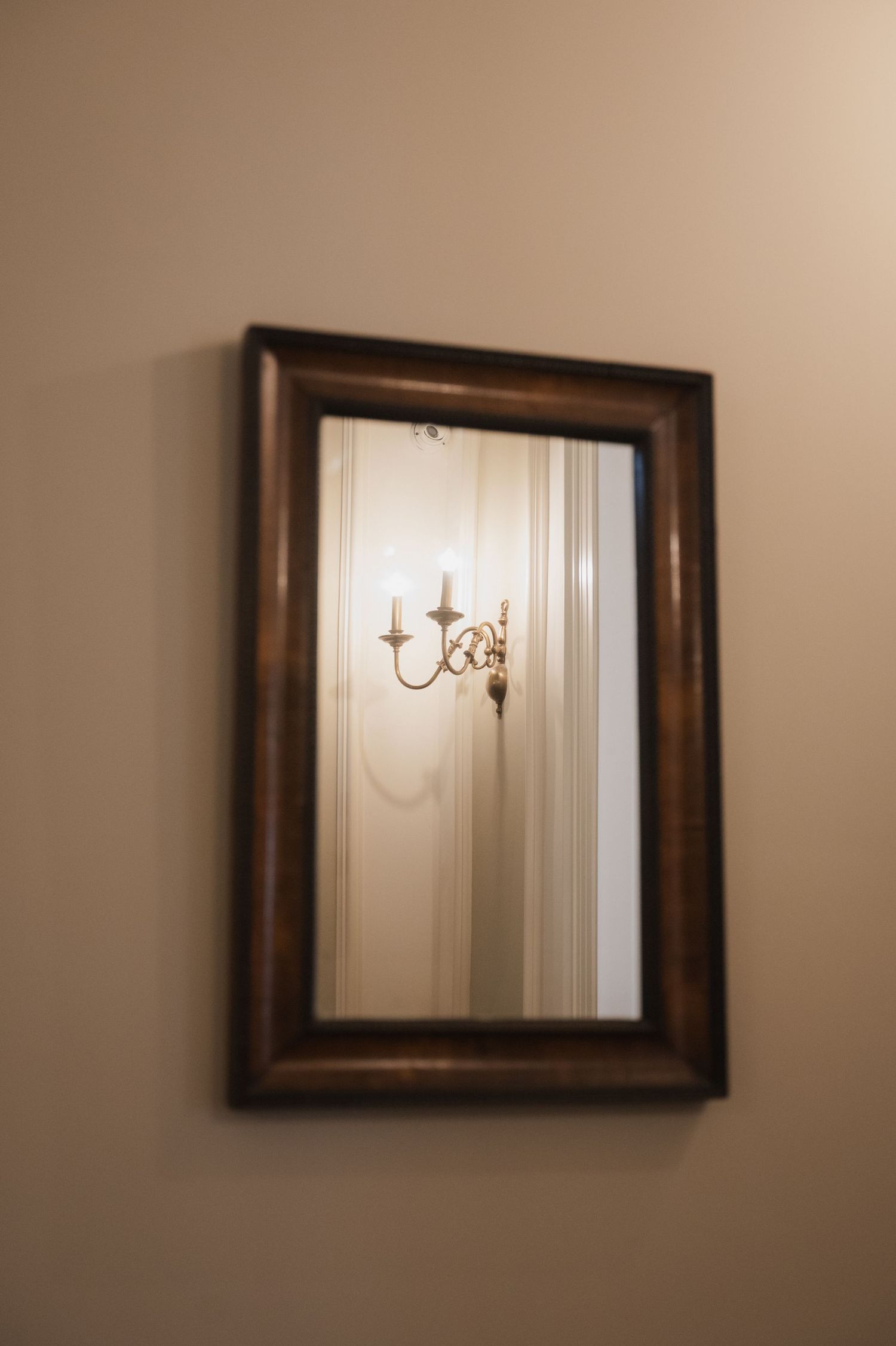 Ornate dark wood framed mirror on beige wall reflecting elegant candle wall sconce.