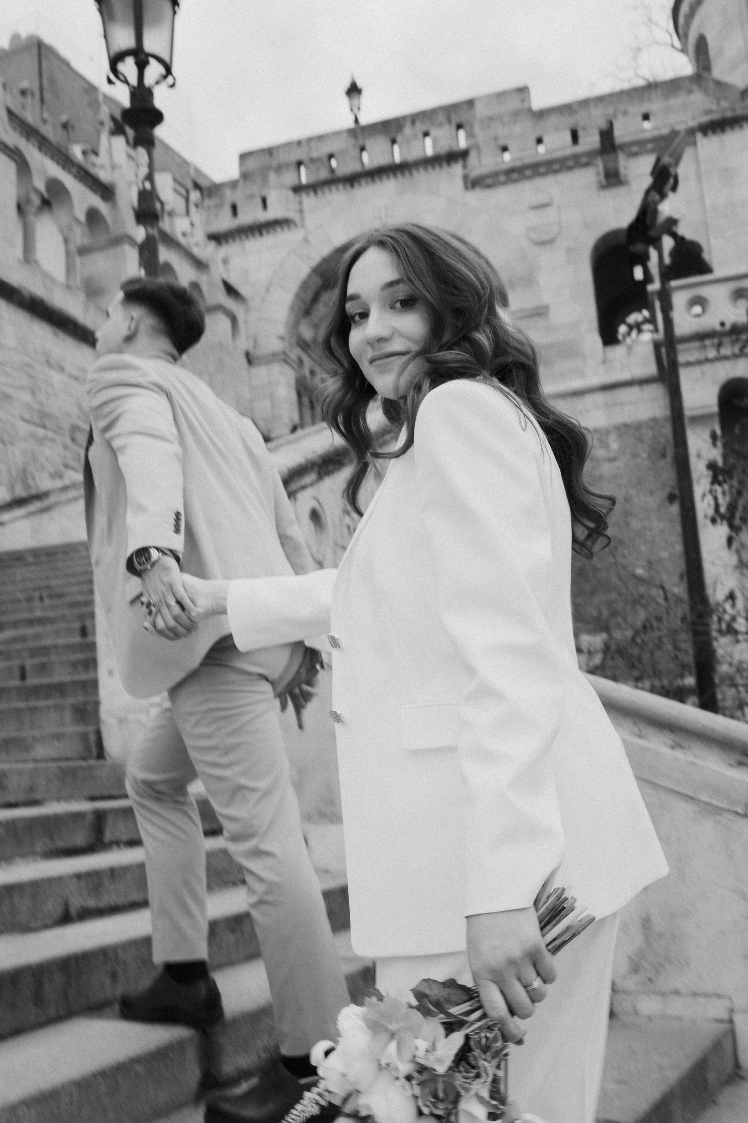 A woman wearing a white dress stands on steps, smiling at the camera in a black and white photograph.