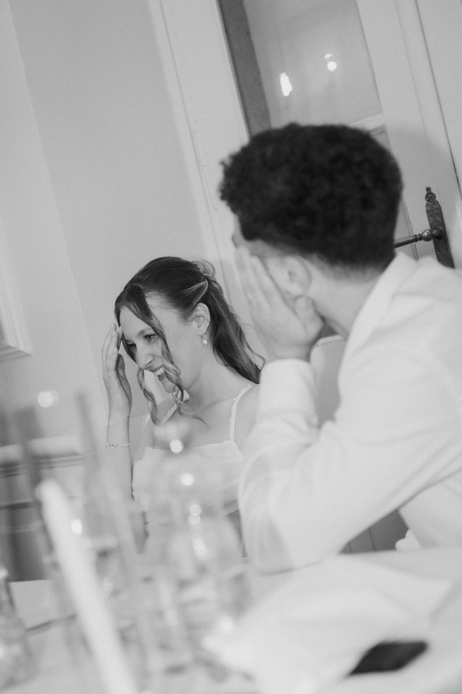 Black and white candid photo of emotional bride and groom wiping tears during heartfelt wedding reception moment.