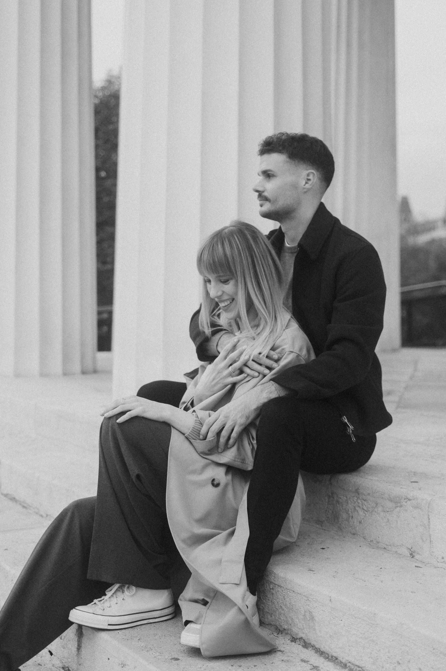 A couple sits intimately on white stone steps in a black and white artistic portrait.