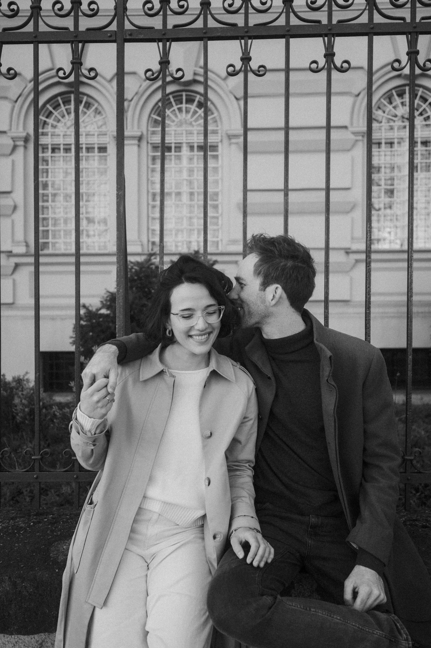 A romantic black and white photo series showing a couple laughing and embracing by an ornate iron gate.
