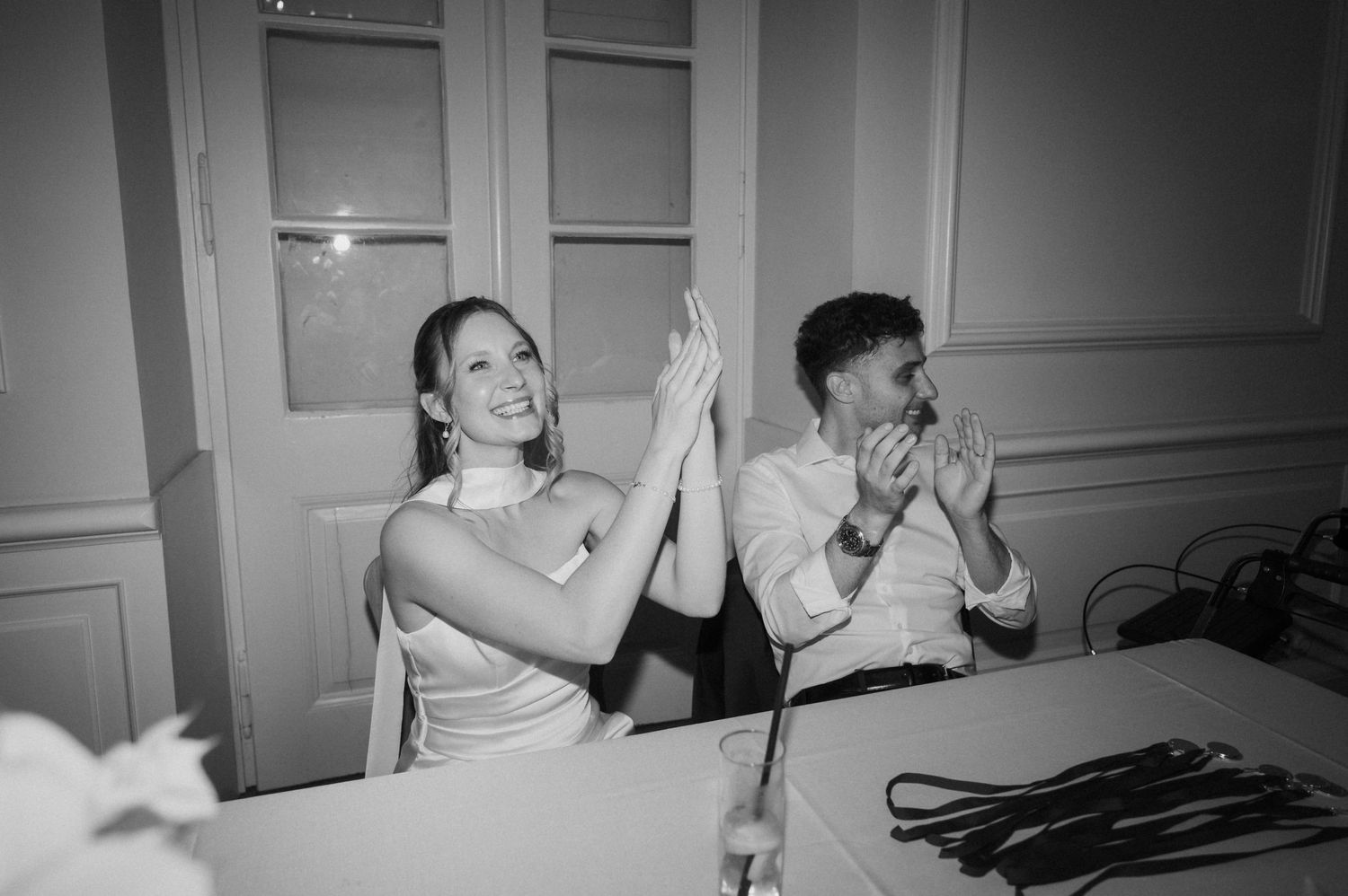 Black and white photo of bride and groom clapping and laughing together at their wedding reception.
