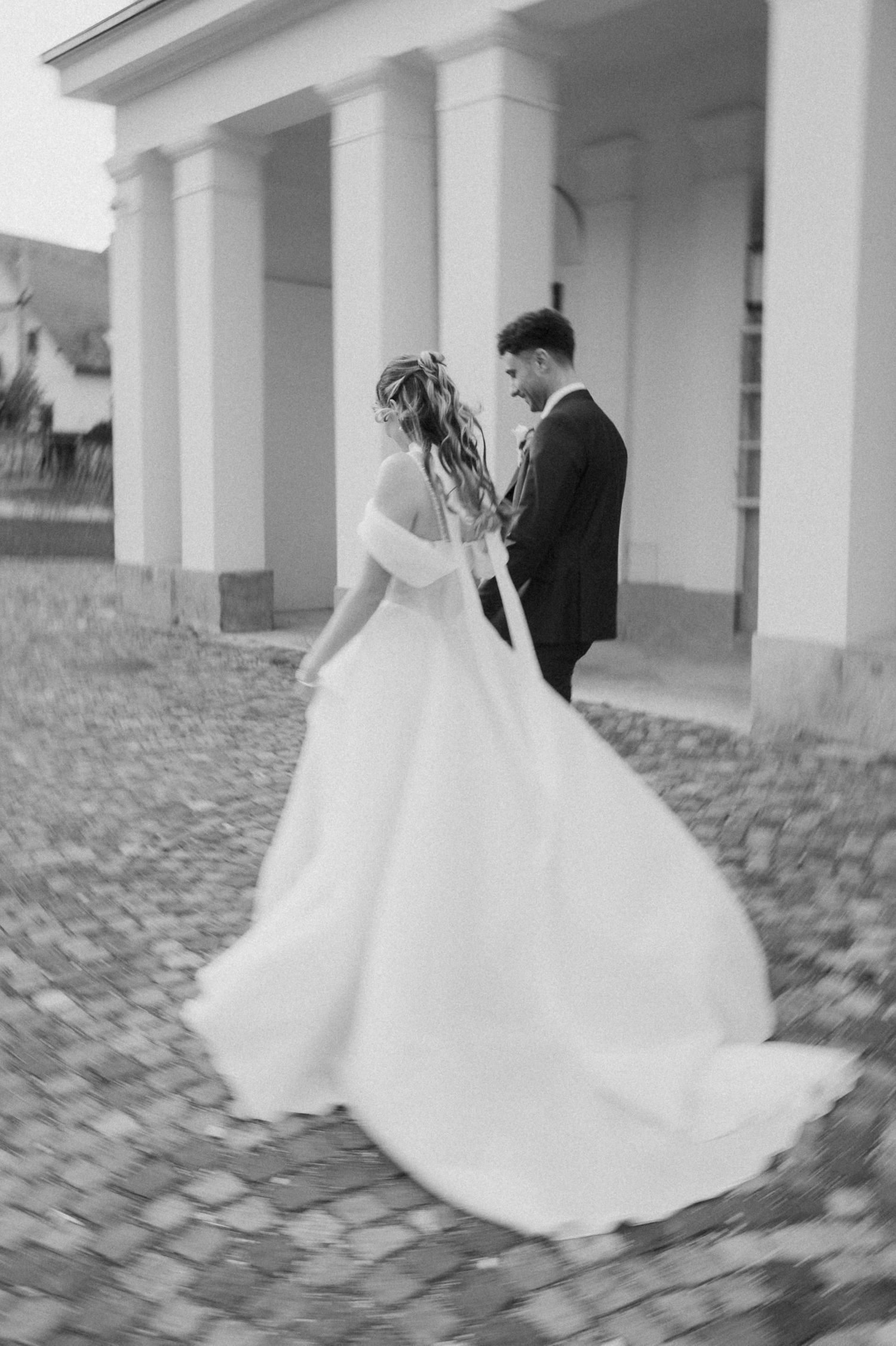 Bride and groom share a romantic moment in black and white photo outside columned building.