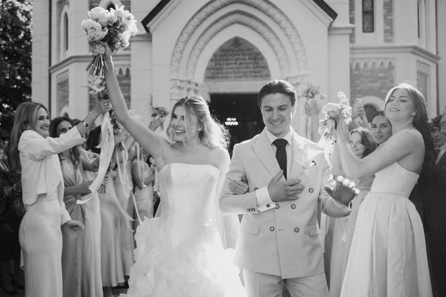Bride and groom celebrating outside a church after wedding ceremony in black and white photo.