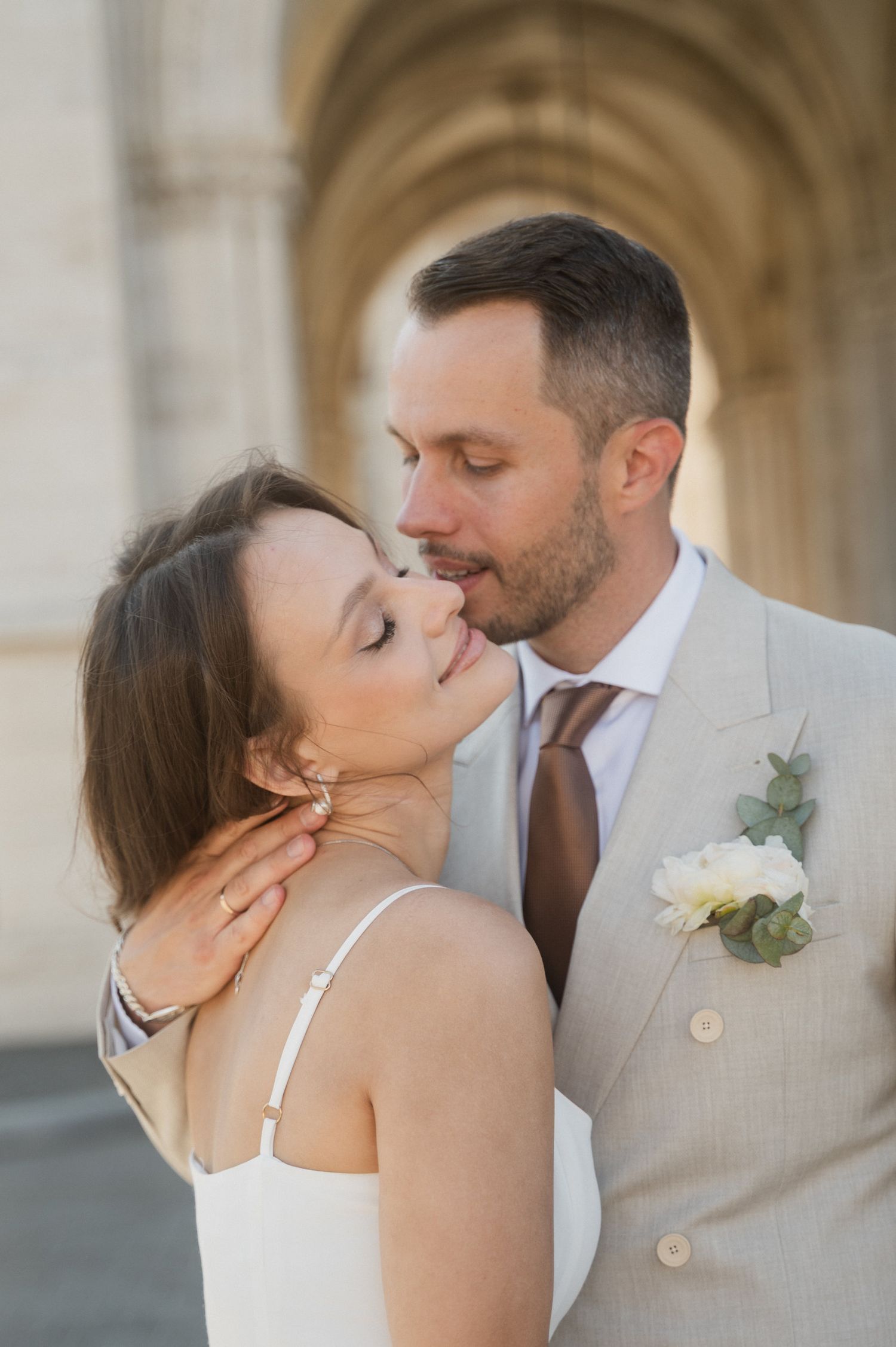 A romantic wedding couple shares an intimate moment in front of an ornate archway.
