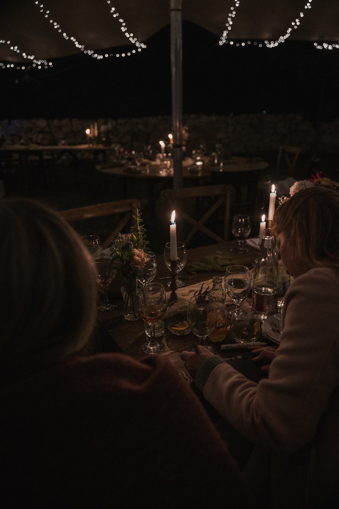 Candlelit outdoor reception tables under string lights create romantic evening ambiance.