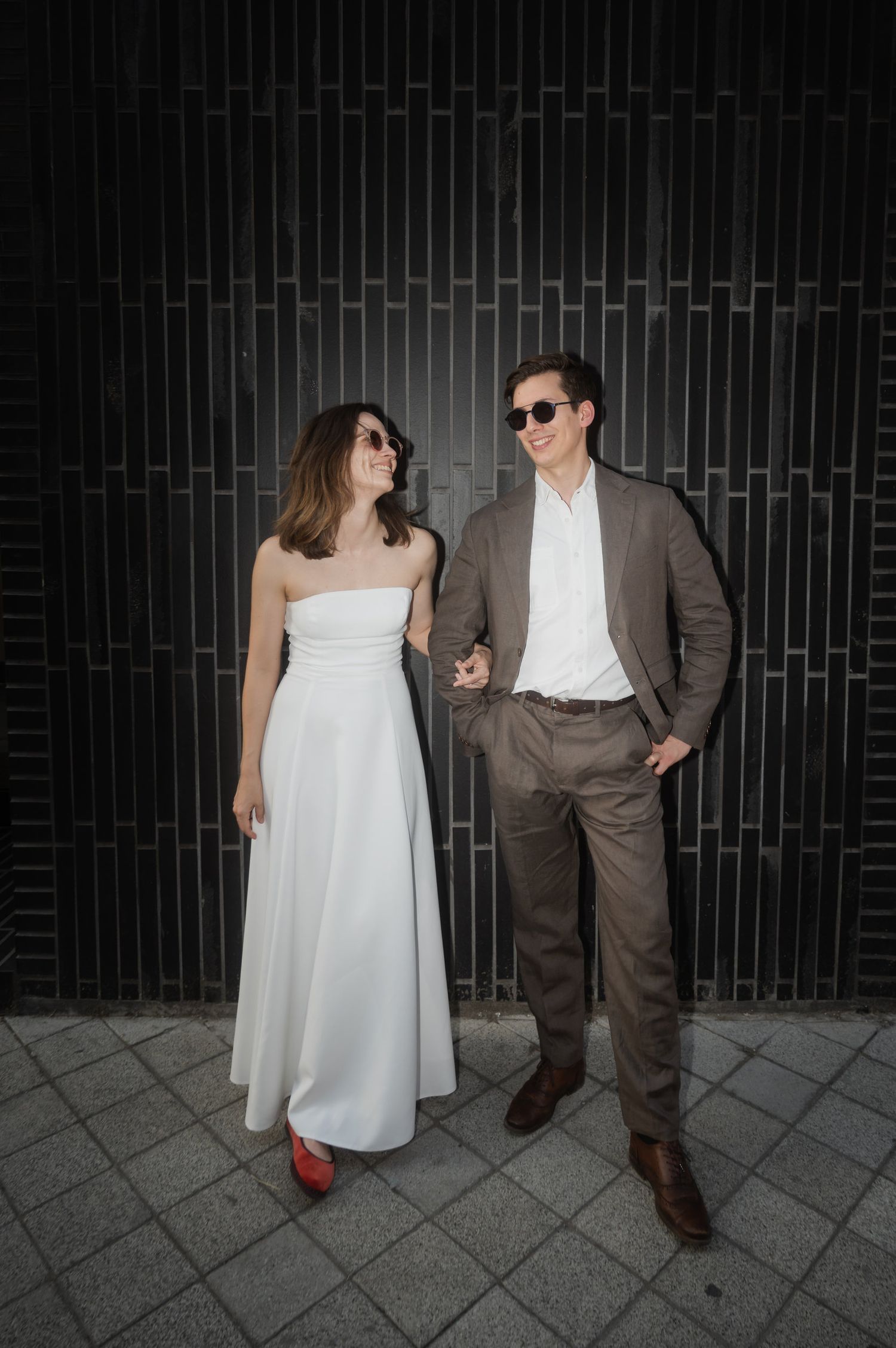 A stylish couple poses against a dark wall, creating a modern urban fashion scene.