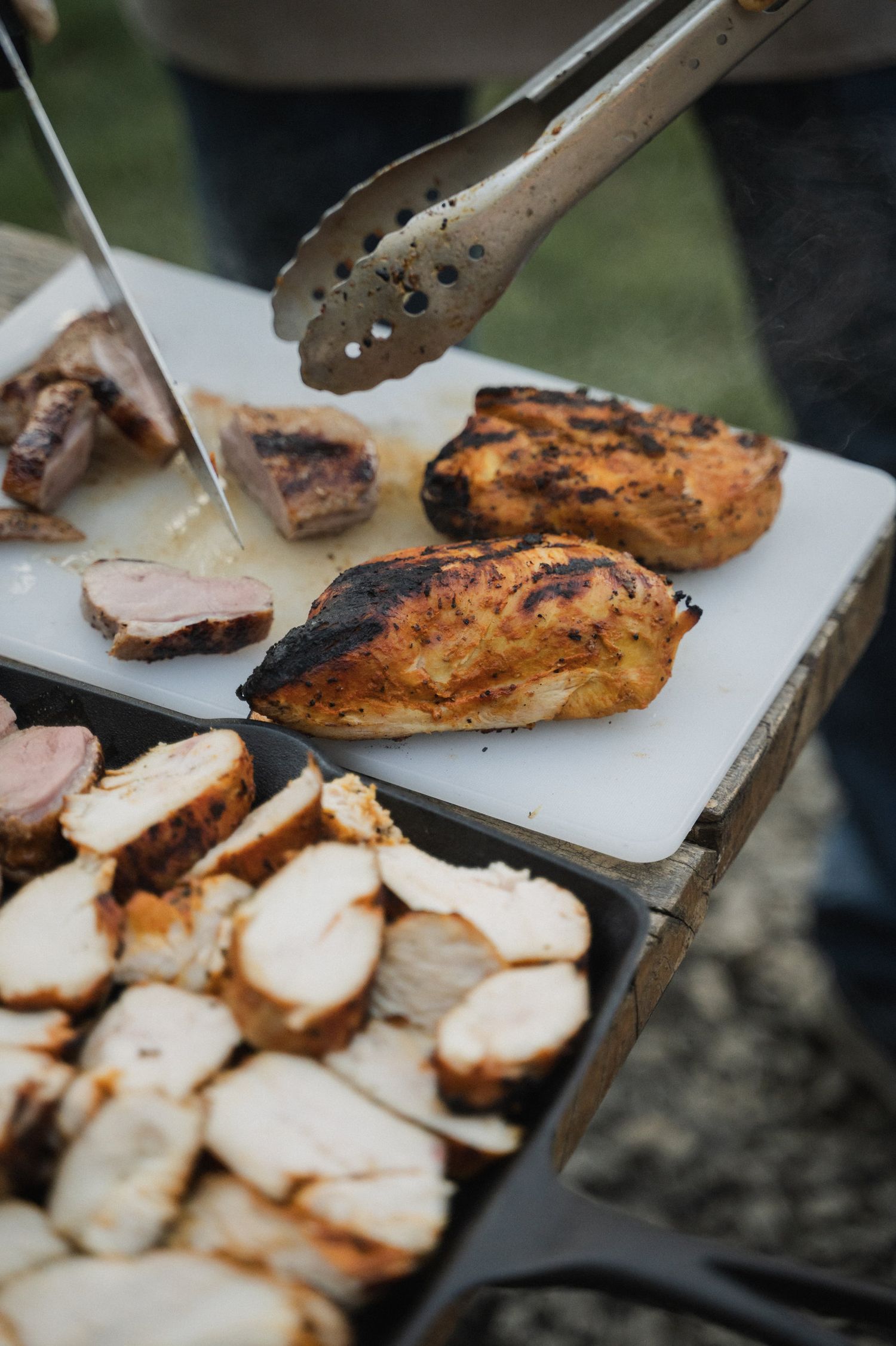 Grilled chicken breasts being served with tongs on a white cutting board, showing sliced portions.