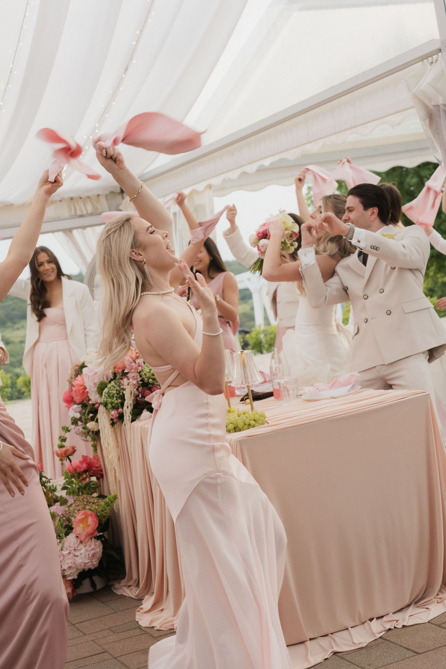 Bride in white gown celebrates with bridesmaids and guests under a decorated wedding reception tent.