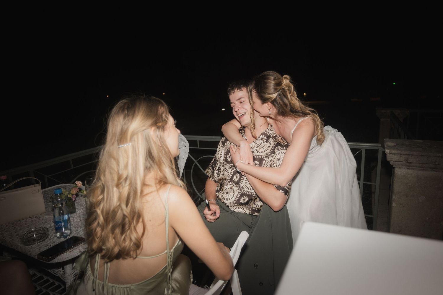 Bride in white gown embraces guests during an outdoor evening wedding reception.