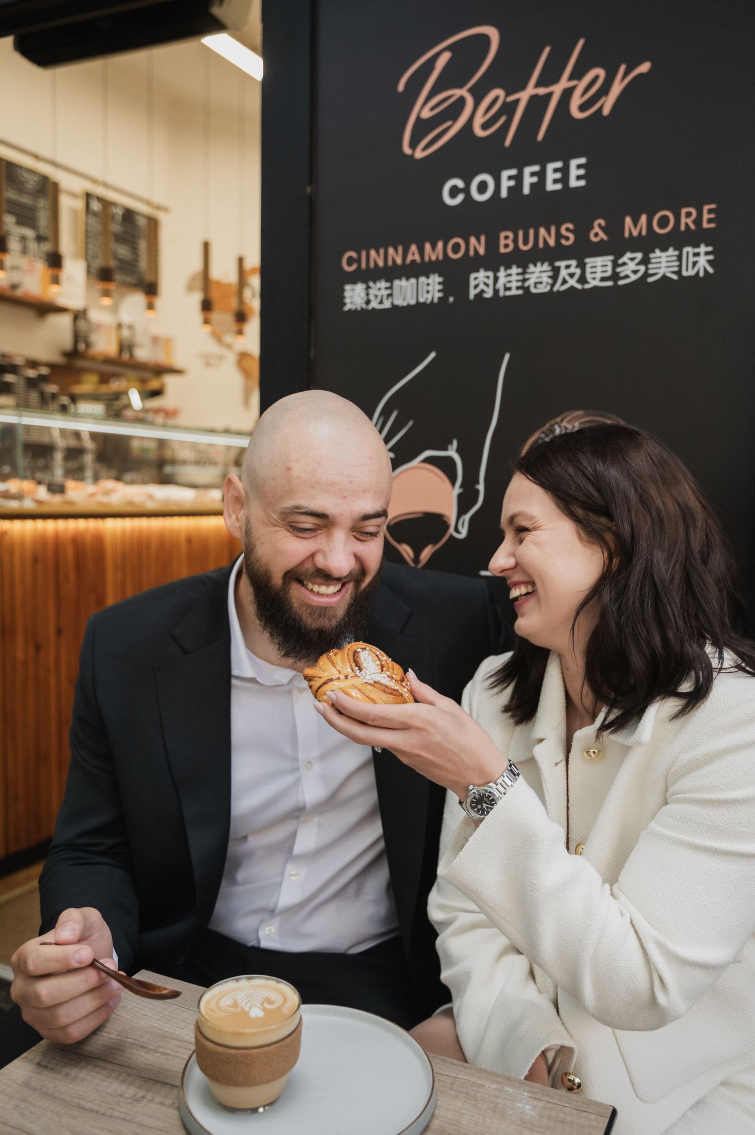 A couple shares a joyful moment at Better Coffee shop while enjoying cinnamon buns and coffee.