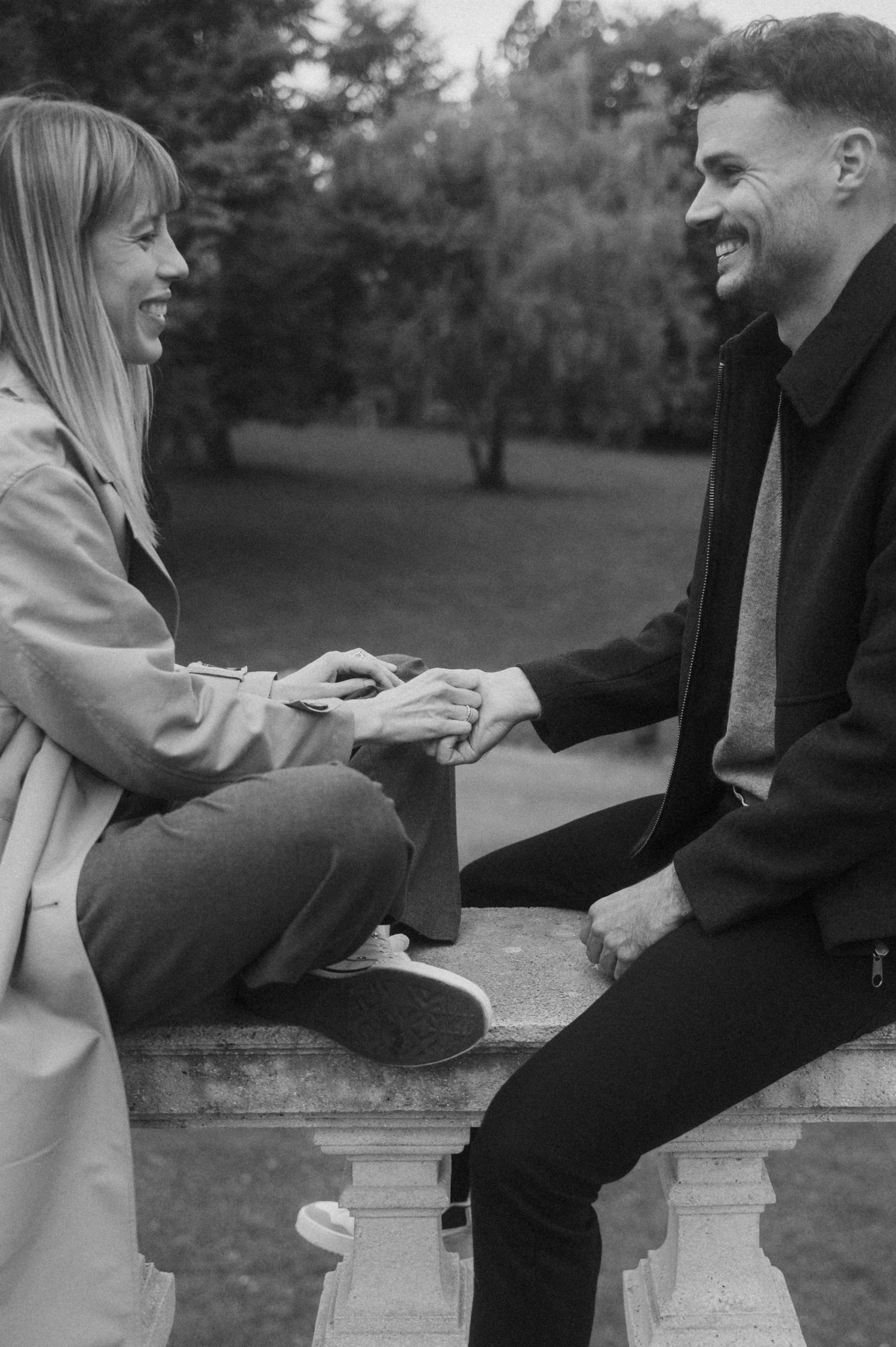 A couple sits together on a stone ledge in a park sharing intimate moments in black and white photography.