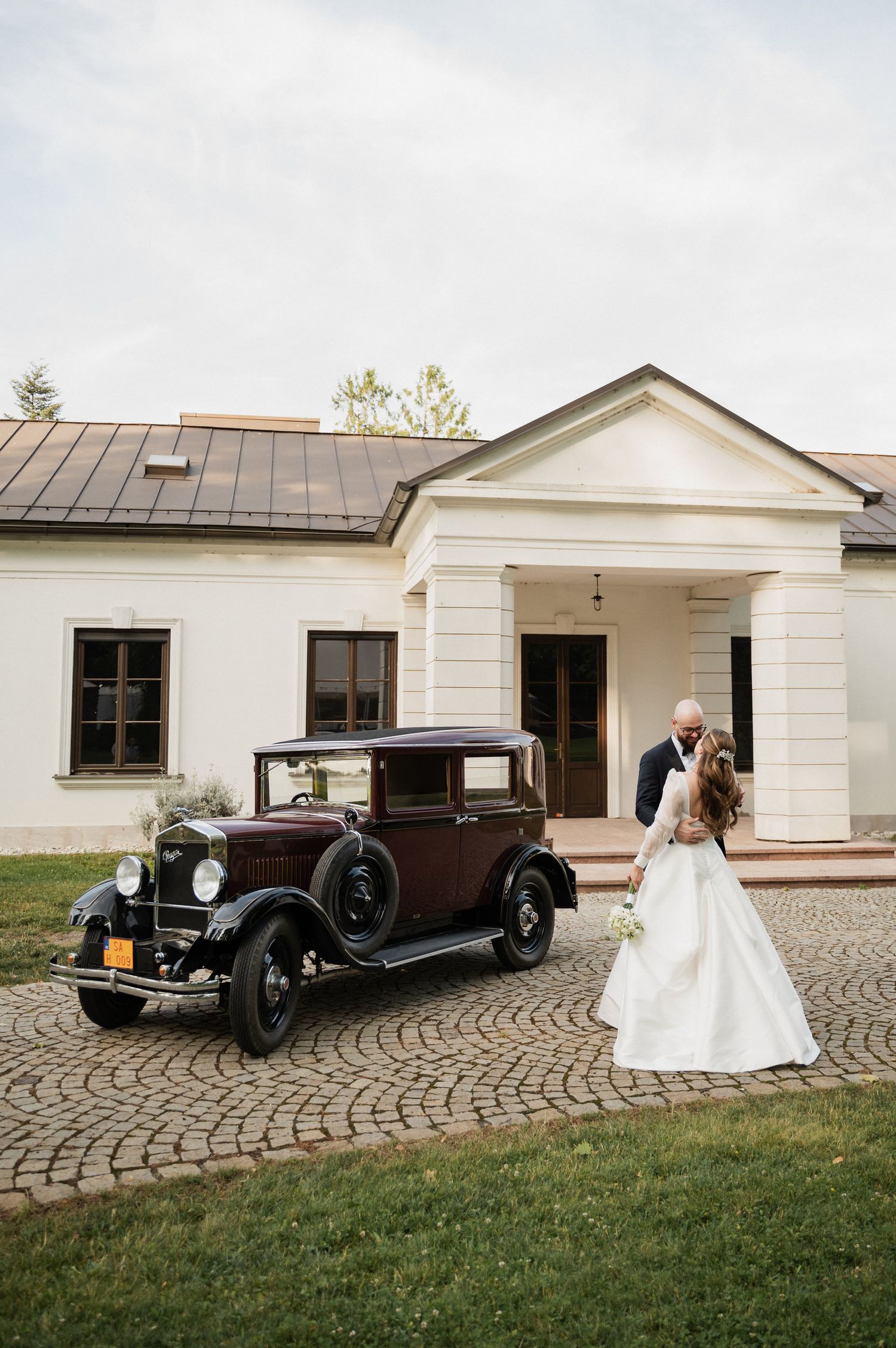 A vintage black classic car parked outside a white building with a cobblestone driveway.