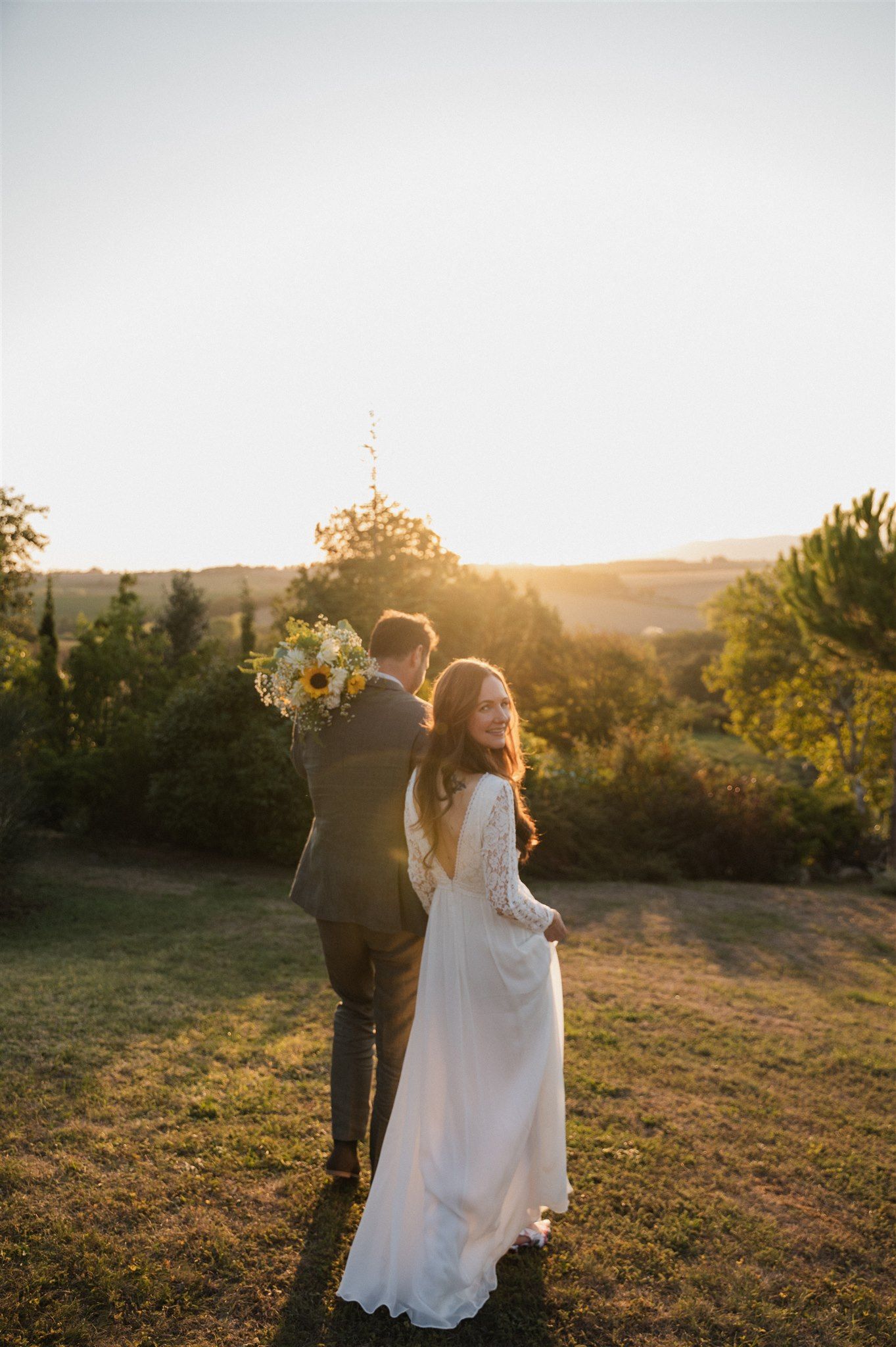 A couple embraces during golden hour with sunlit flowers and rolling hills in background.